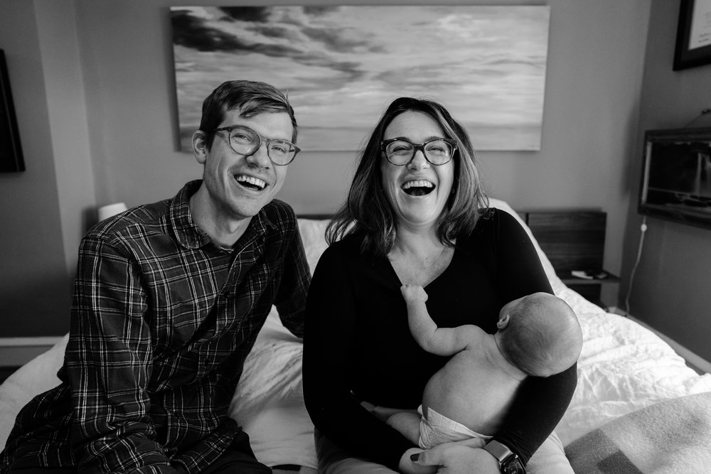 Joyful black and white portrait of happy, laughing parents with baby on bed, Philadelphia newborn photography