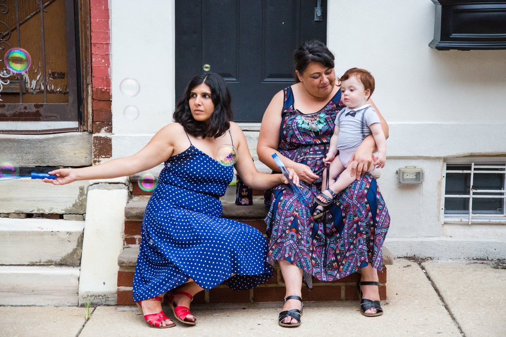 Candid moment, wedding guests, women with baby on south philly stoop blowing bubbles, Philadelphia documentary photographer