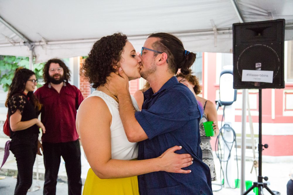 Groom and bride kiss under reception tent with smiling guests, Philly wedding photography