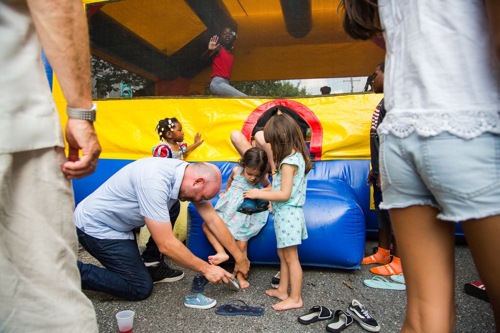 Dad helps kids take off shoes for bounce house at block party reception, Philadelphia wedding photographer
