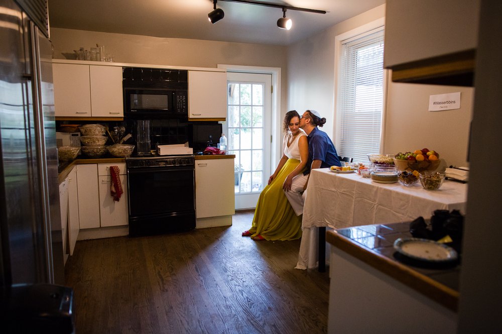 Groom gives bride a kiss in quiet moment before wedding ceremony, in kitchen childhood south philly home, documentary photographer