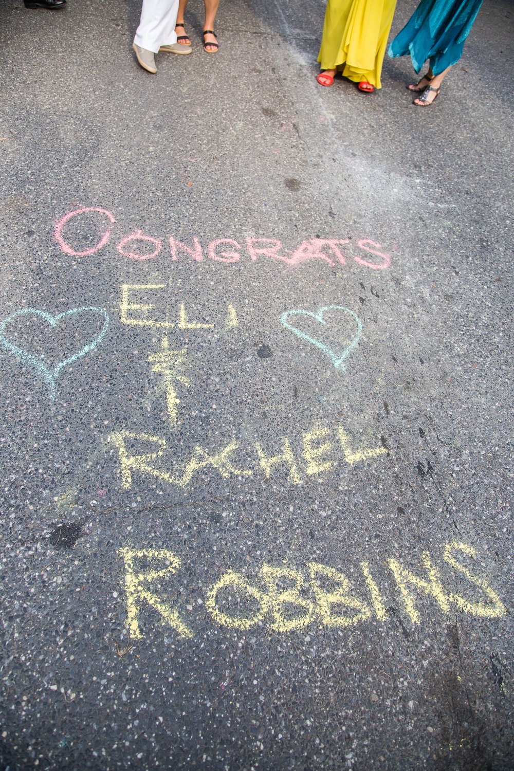 Chalk art on street pavement celebrating wedding couple, guests feet in background, Philly documentary photography