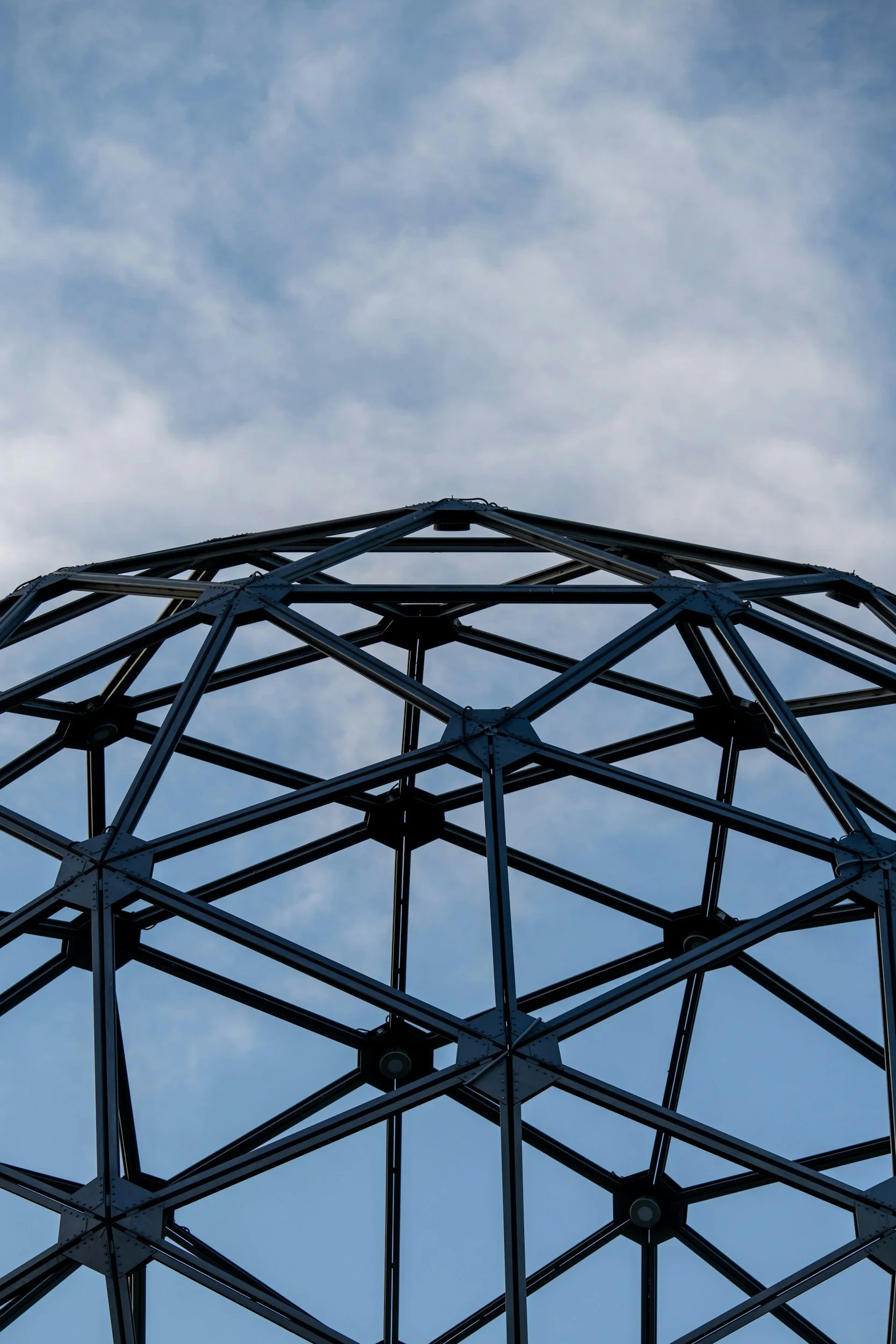 Close-up of a metallic lattice structure with a cloudy sky in the background.