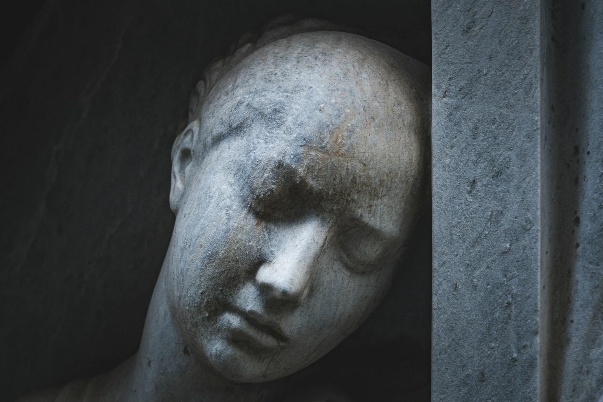 Close-up of an ancient stone sculpture of a human face, with detailed features and weathered surface, partially embedded in a stone wall.