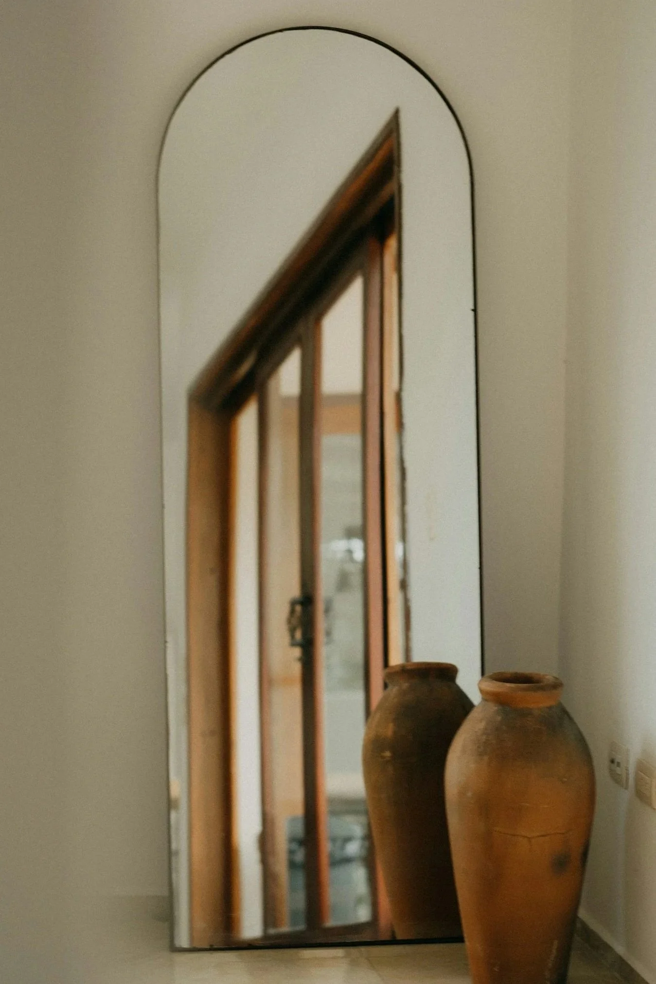A mirror on a wall reflecting a staircase. Two large earthenware pots are in front of the mirror.