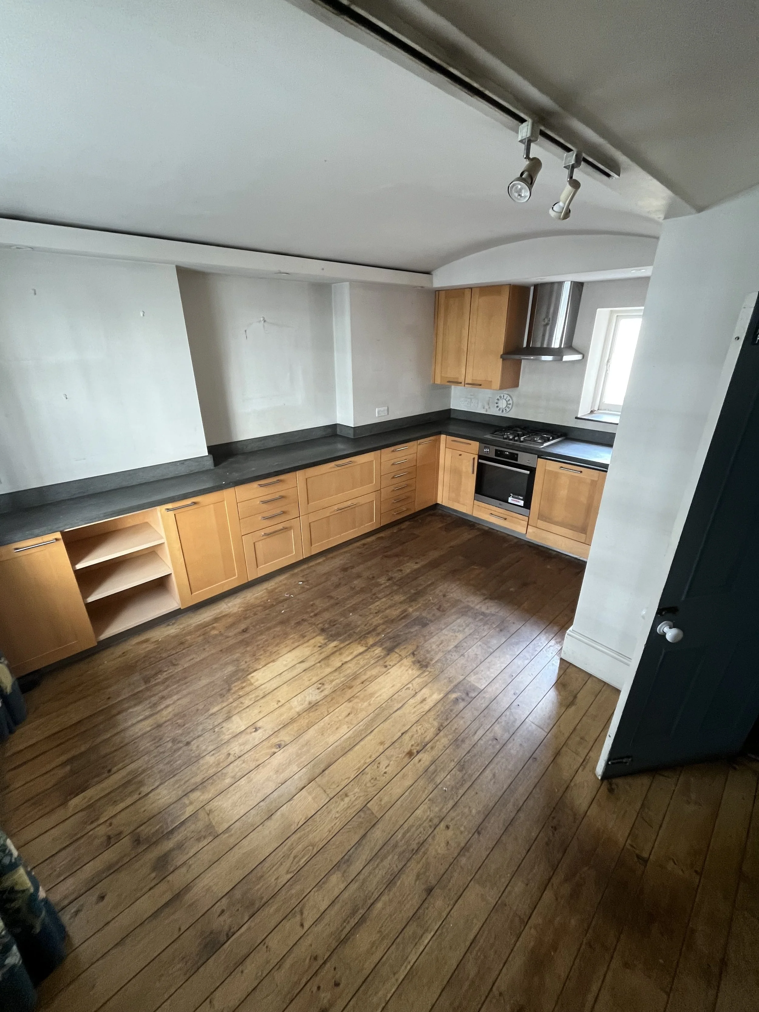 Empty kitchen with wooden cabinets, dark countertop, hardwood floor, stove, and small window.
