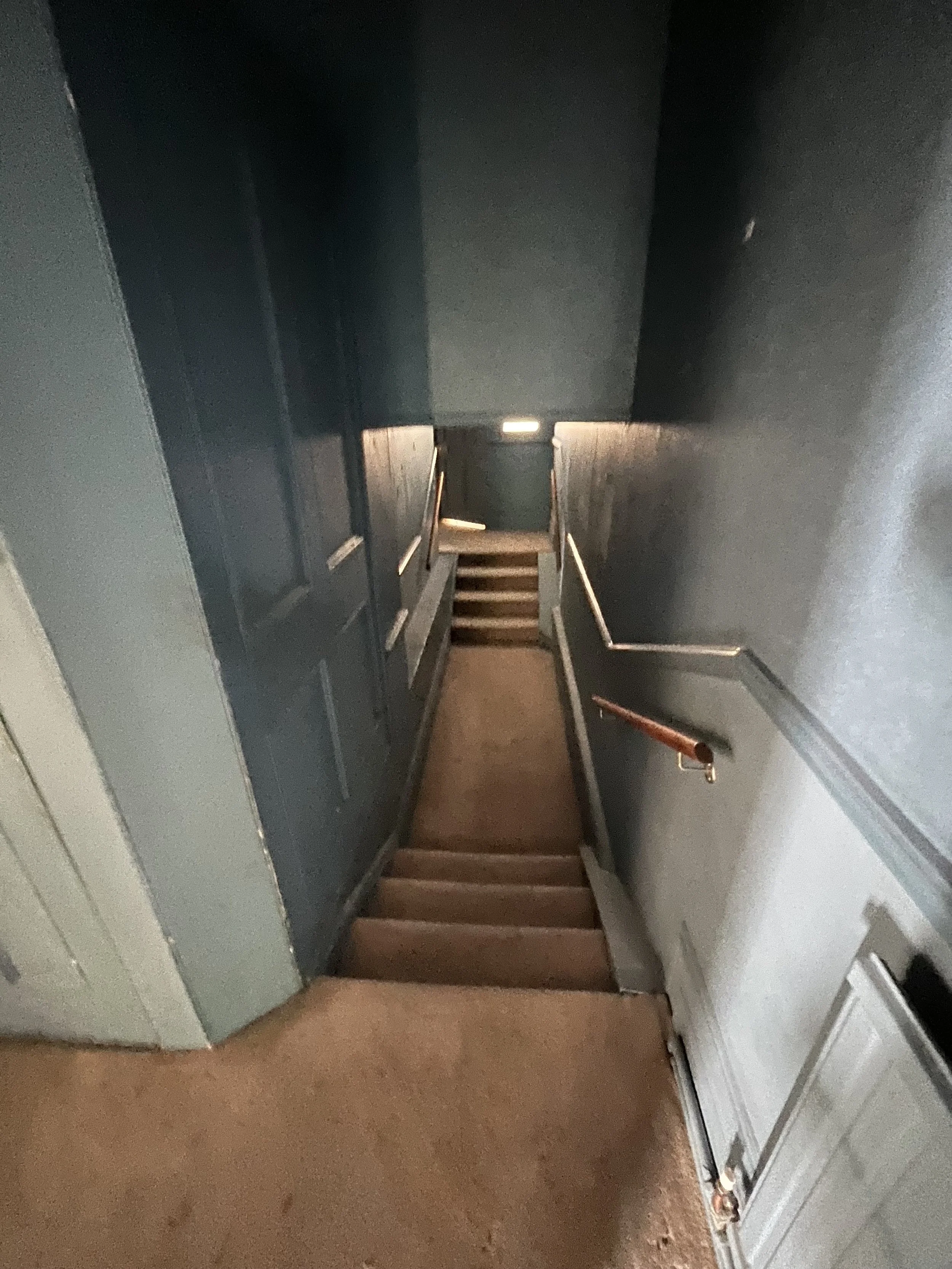 Indoor staircase leading down to a lower level, with dark blue walls and a wooden handrail on the right side.