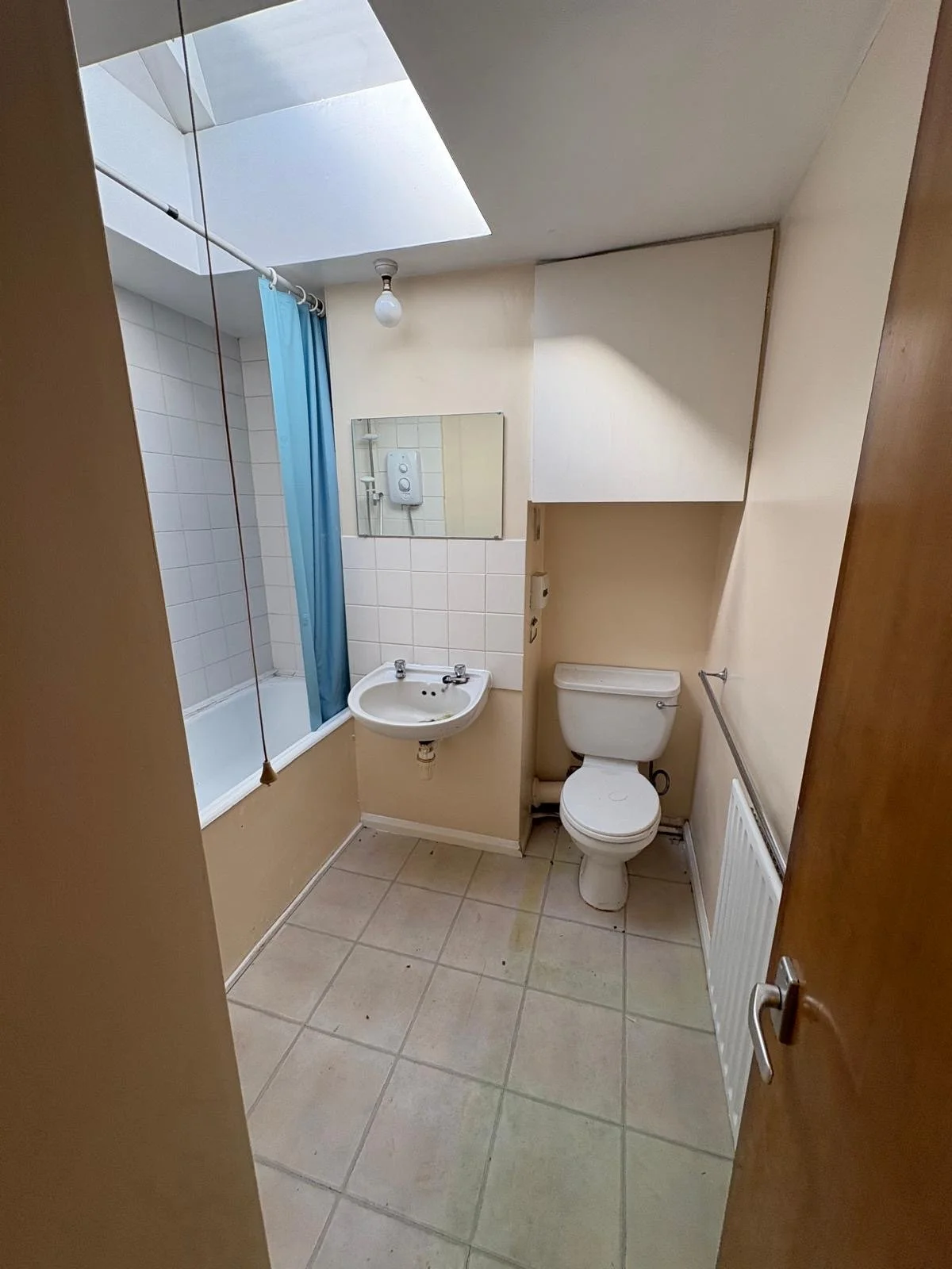 Small bathroom with a bathtub, blue shower curtain, small white sink, toilet, mirror above the sink, tiled floor, and a small radiator.