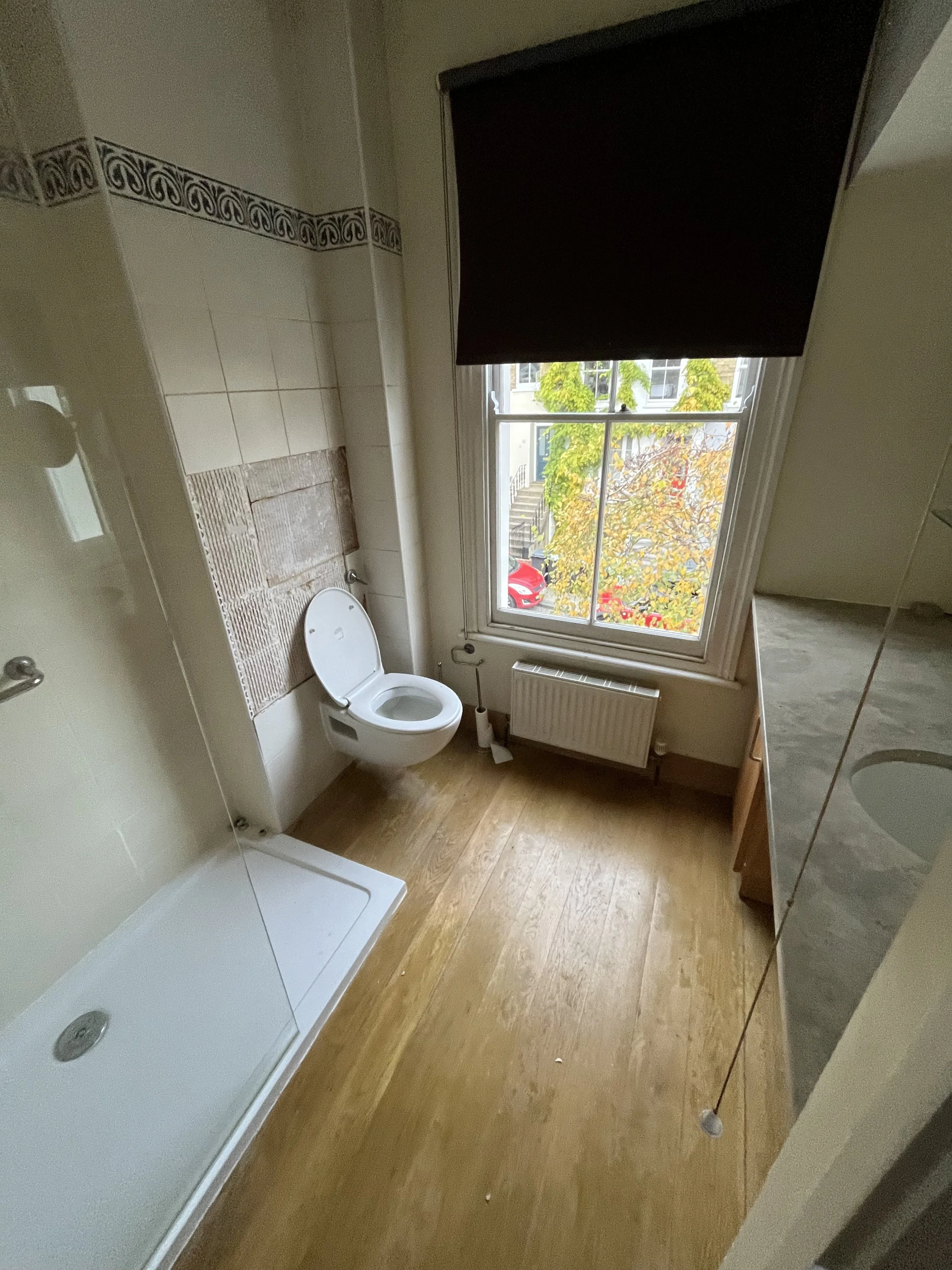 Bathroom with wooden floor, toilet, shower area, window with black blind, and a radiator.