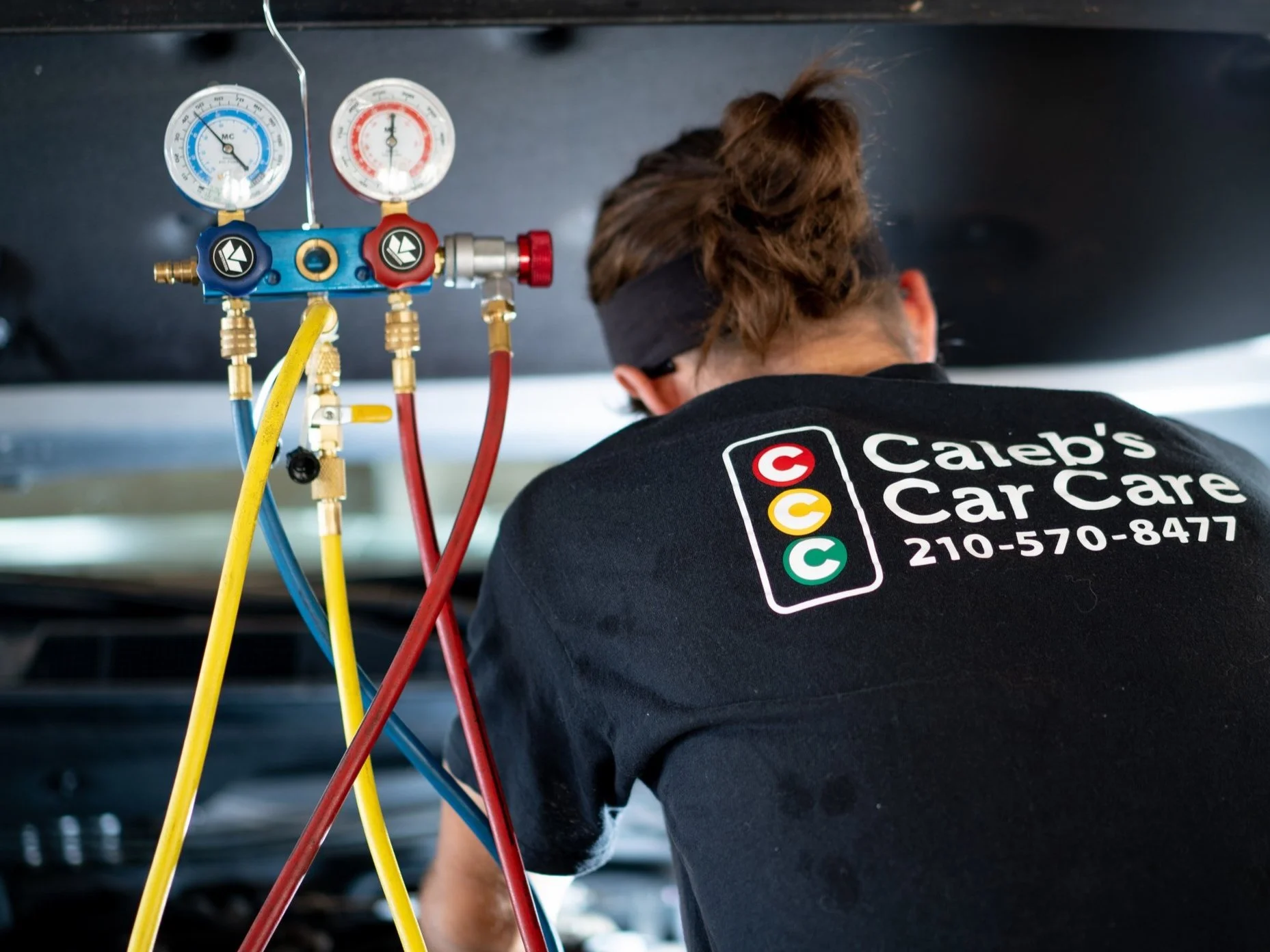 Photo showing technician with gauges connected to an A/C system during a diagnostic.