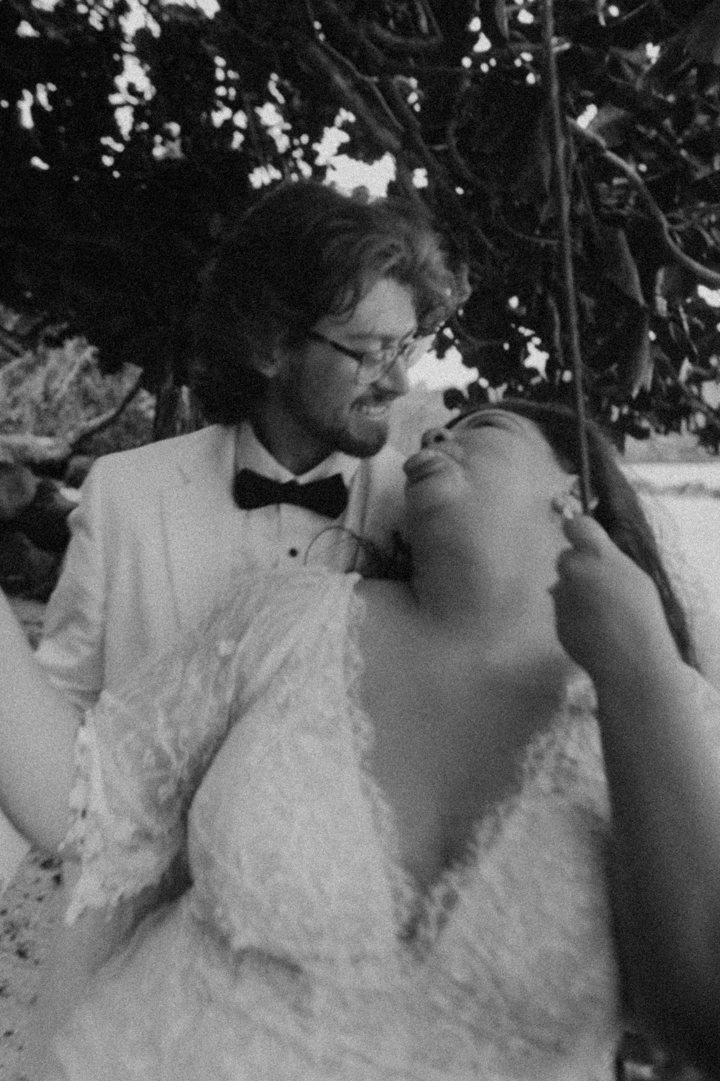 bride and groom cuddling and laughing on a beach swing, sticking their tongues out at each other in kauai in black and white