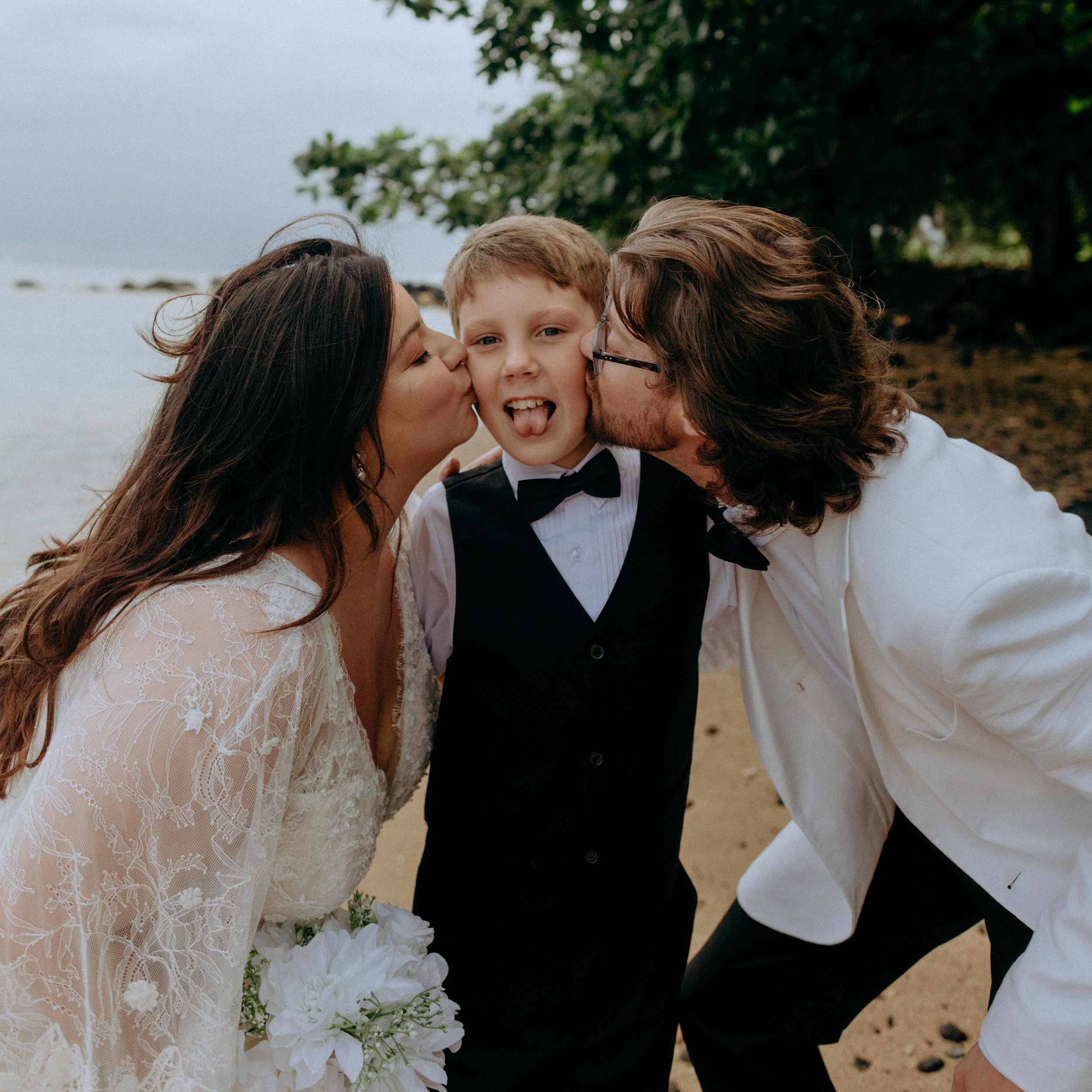 bride and groom kissing their son on the cheek on anini beach, kauai