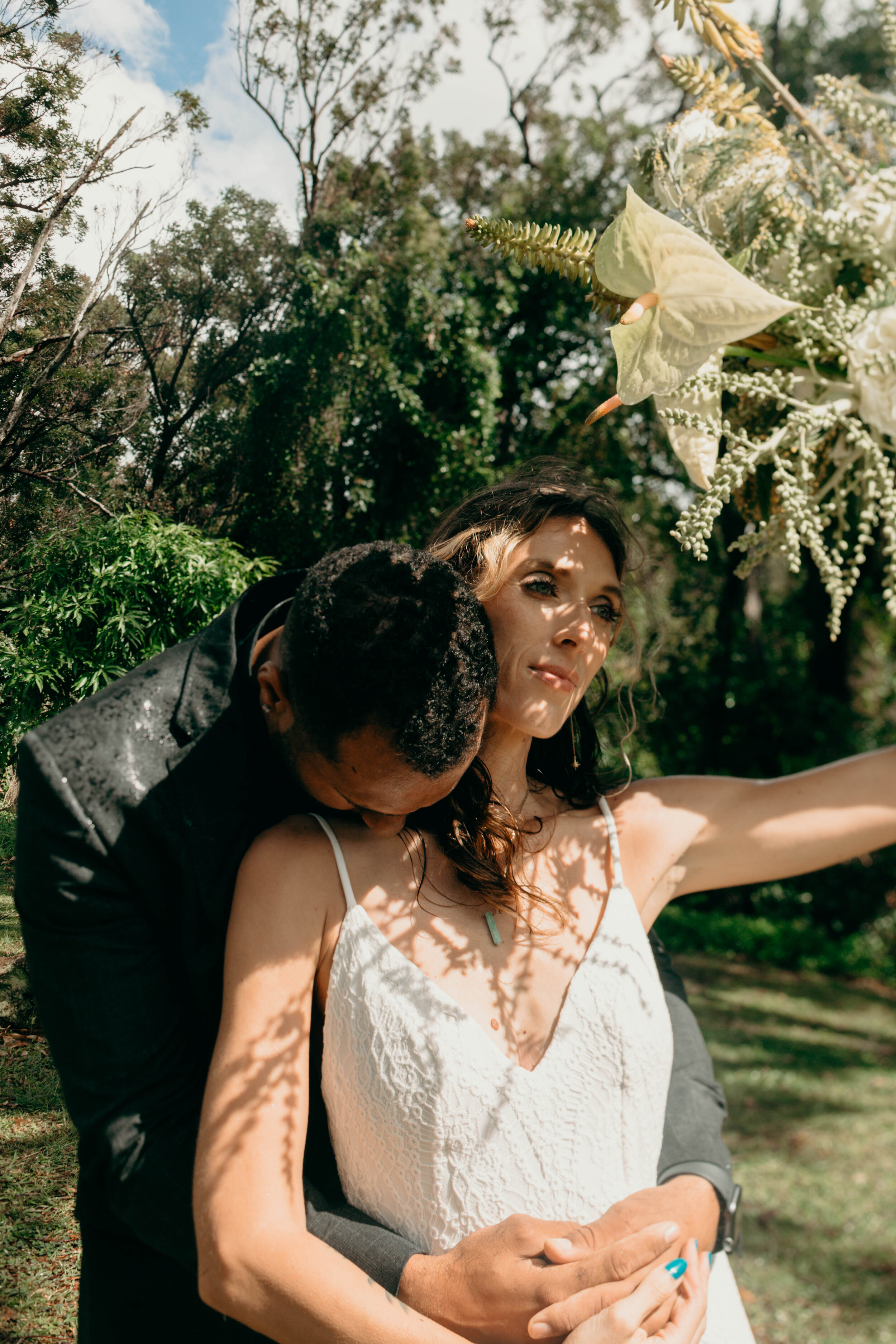 ben kissing dre's neck as she holds her bouquet against the sun