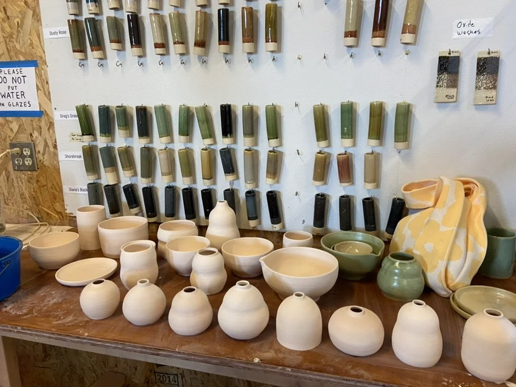 An image of bisque-fired ceramics in front of a wall with glaze samples