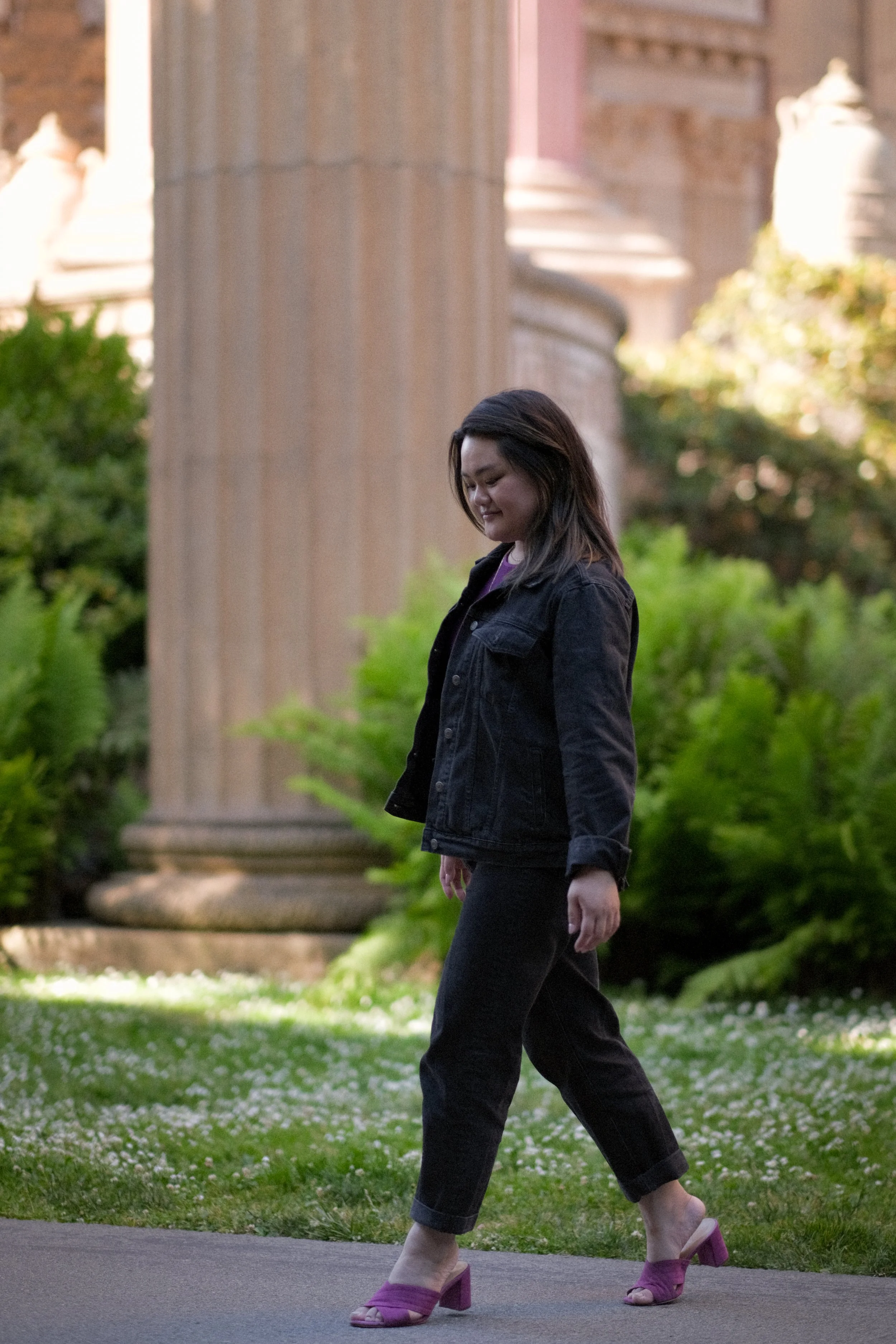 Image of a Taiwanese-American woman wearing a black denim jacket, black jeans, and magenta heeled sandals walking.