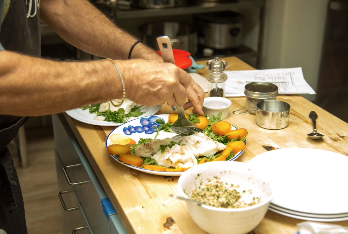 Image of hands plating cod filet onto a bed of arugula and golden beets.