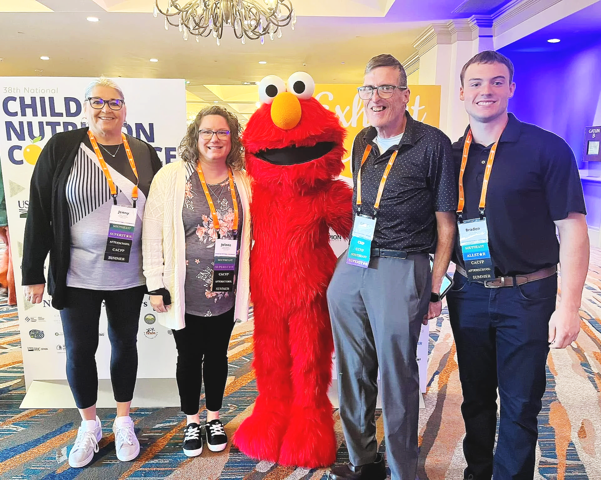 Group of five people and a person in a large Elmo costume posing together at a conference.