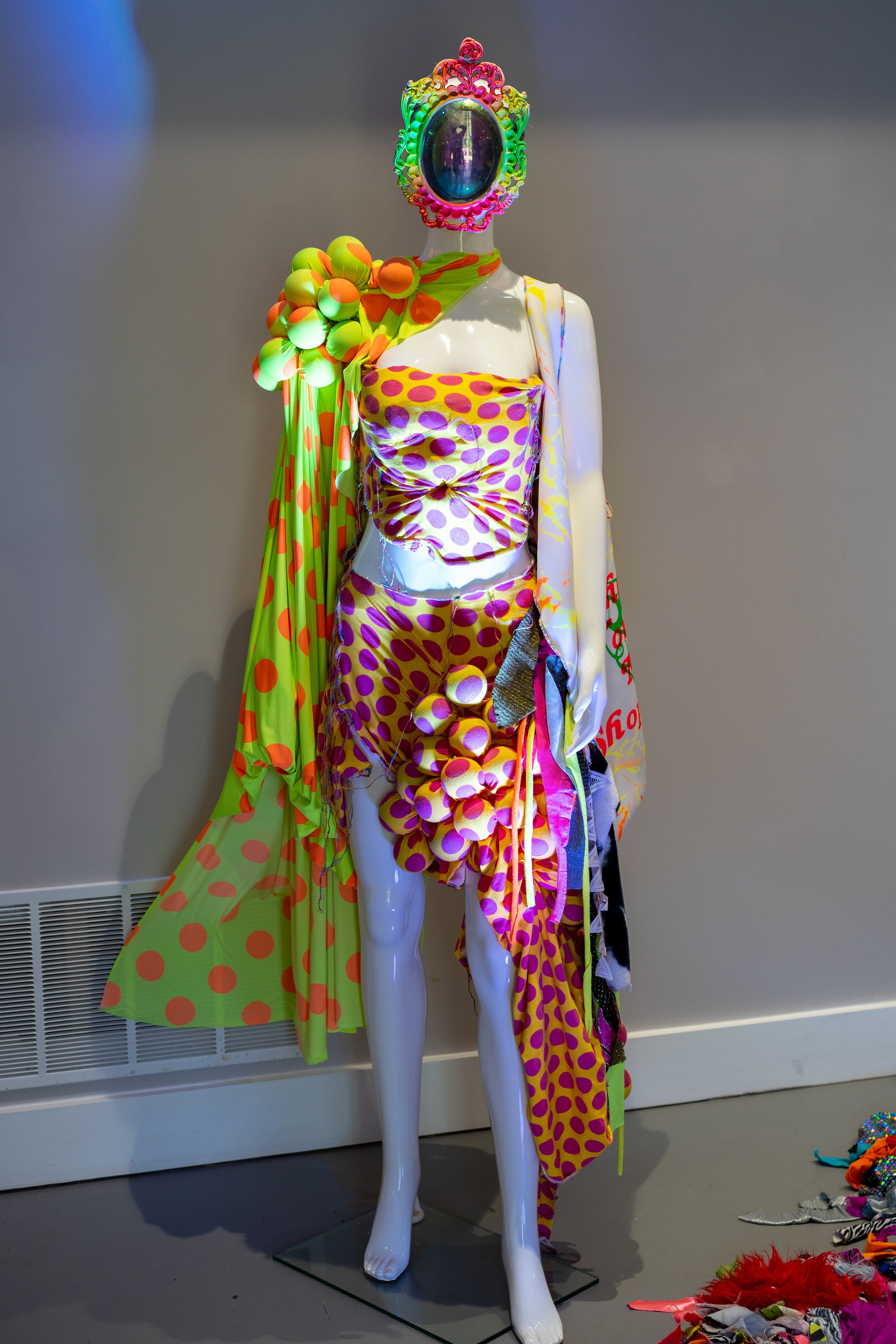 Colorful mannequin wearing a bright polka dot outfit with an ornate, reflective headpiece.