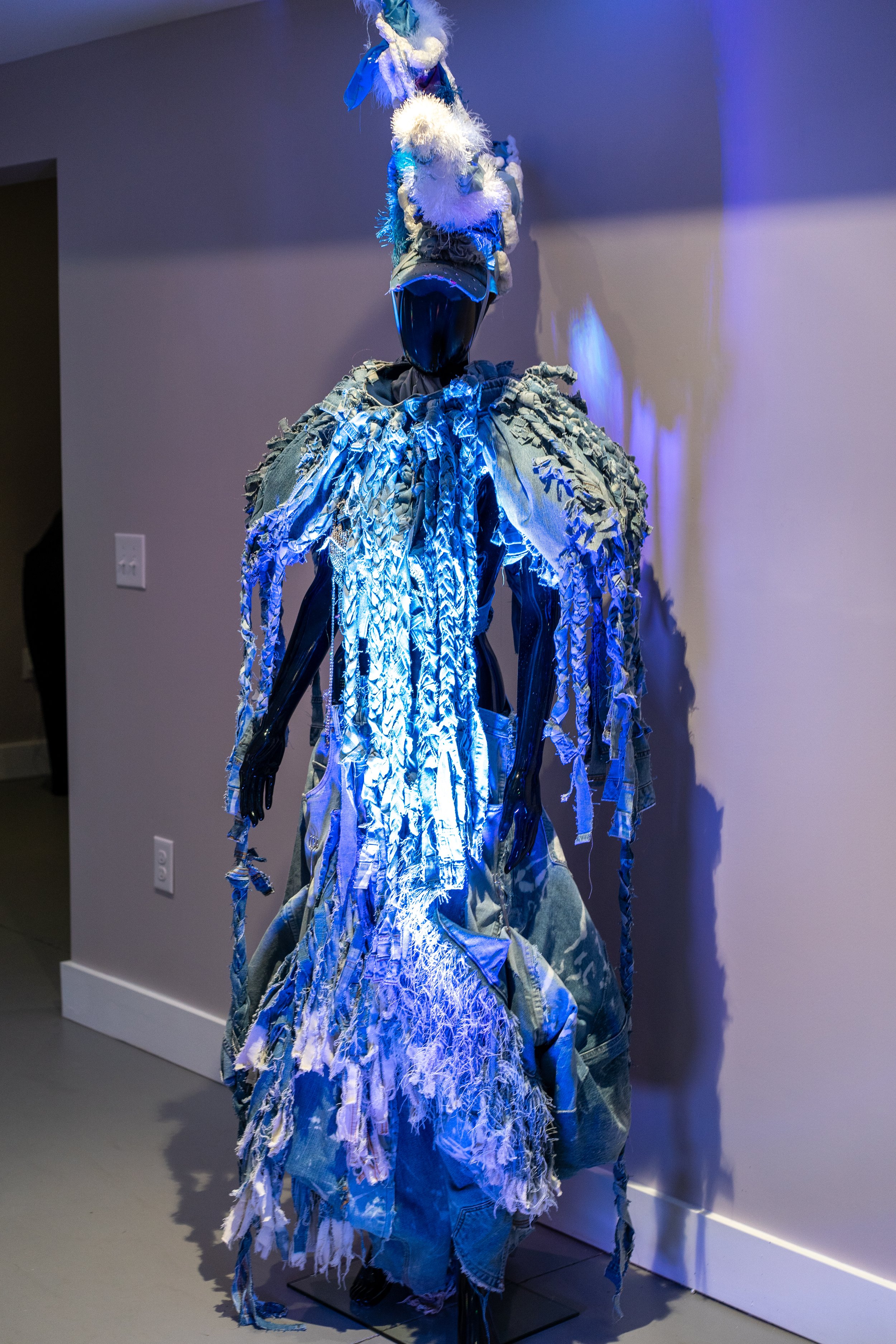 Mannequin wearing a dramatic blue fabric sculpture with shredded denim and textured materials.