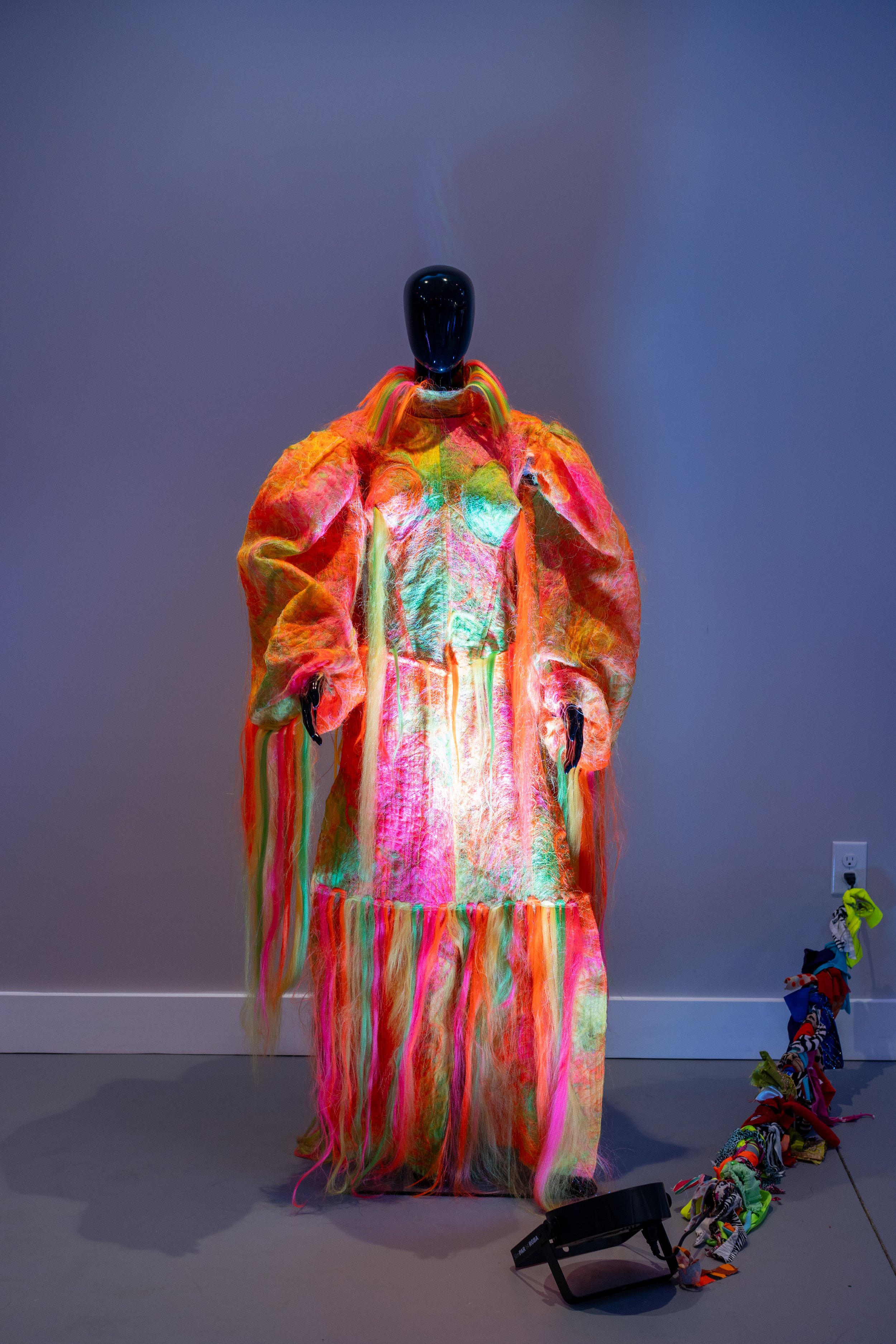 Colorful, textured garment on a mannequin with neon lights.