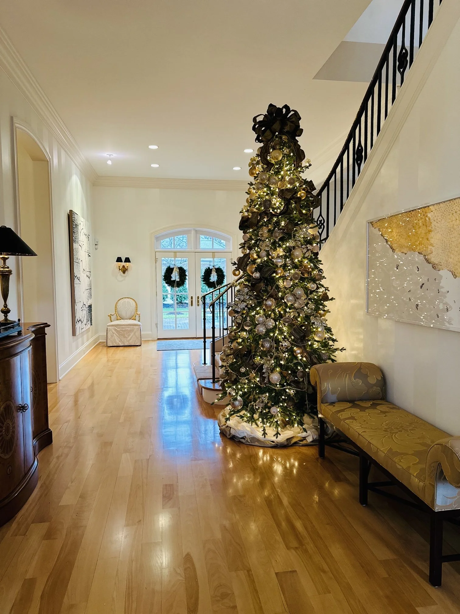 A decorated Christmas tree in a spacious, elegant foyer with hardwood floors and a staircase.