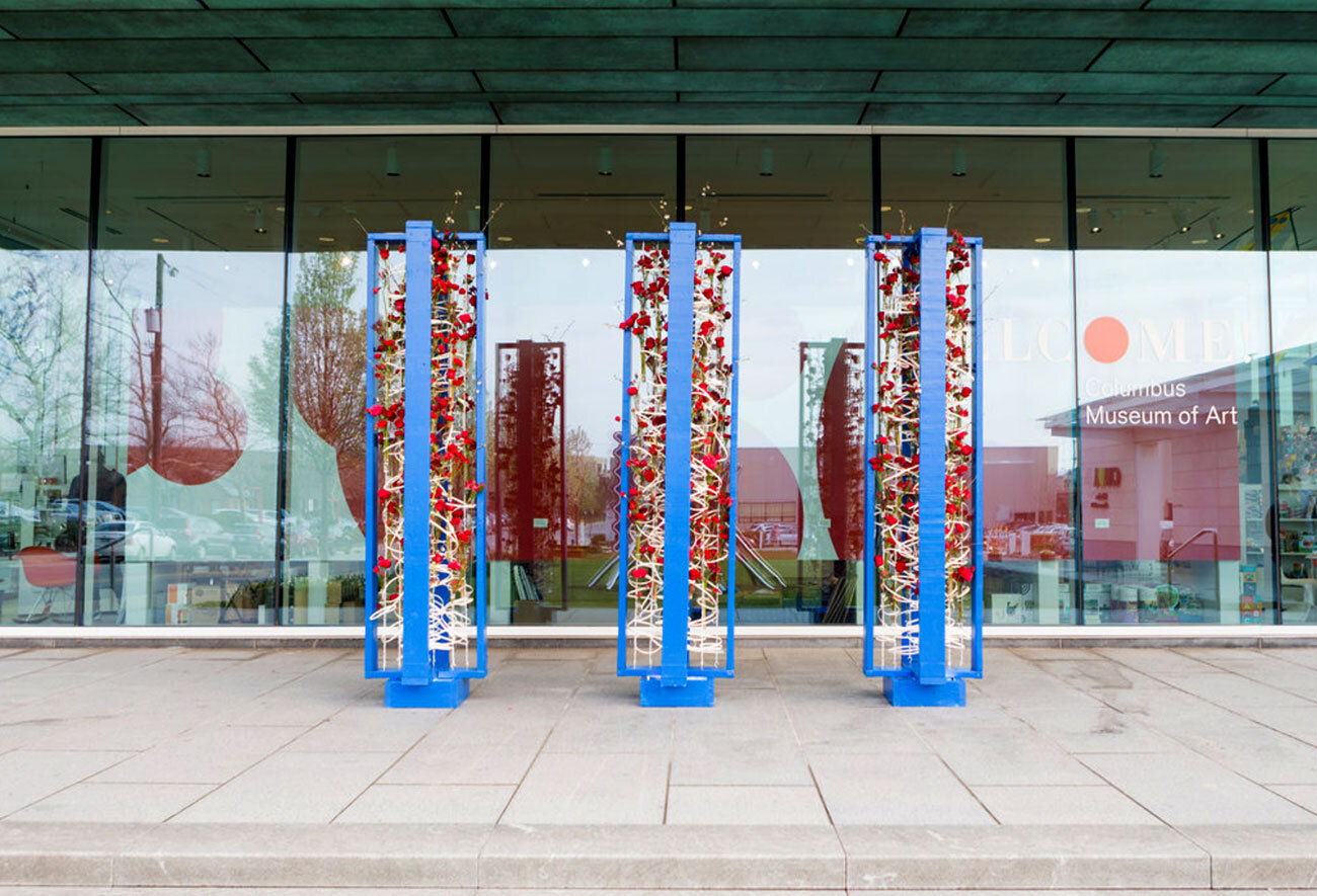 Art installation outside Columbus Museum of Art with blue vertical structures and red flowers.