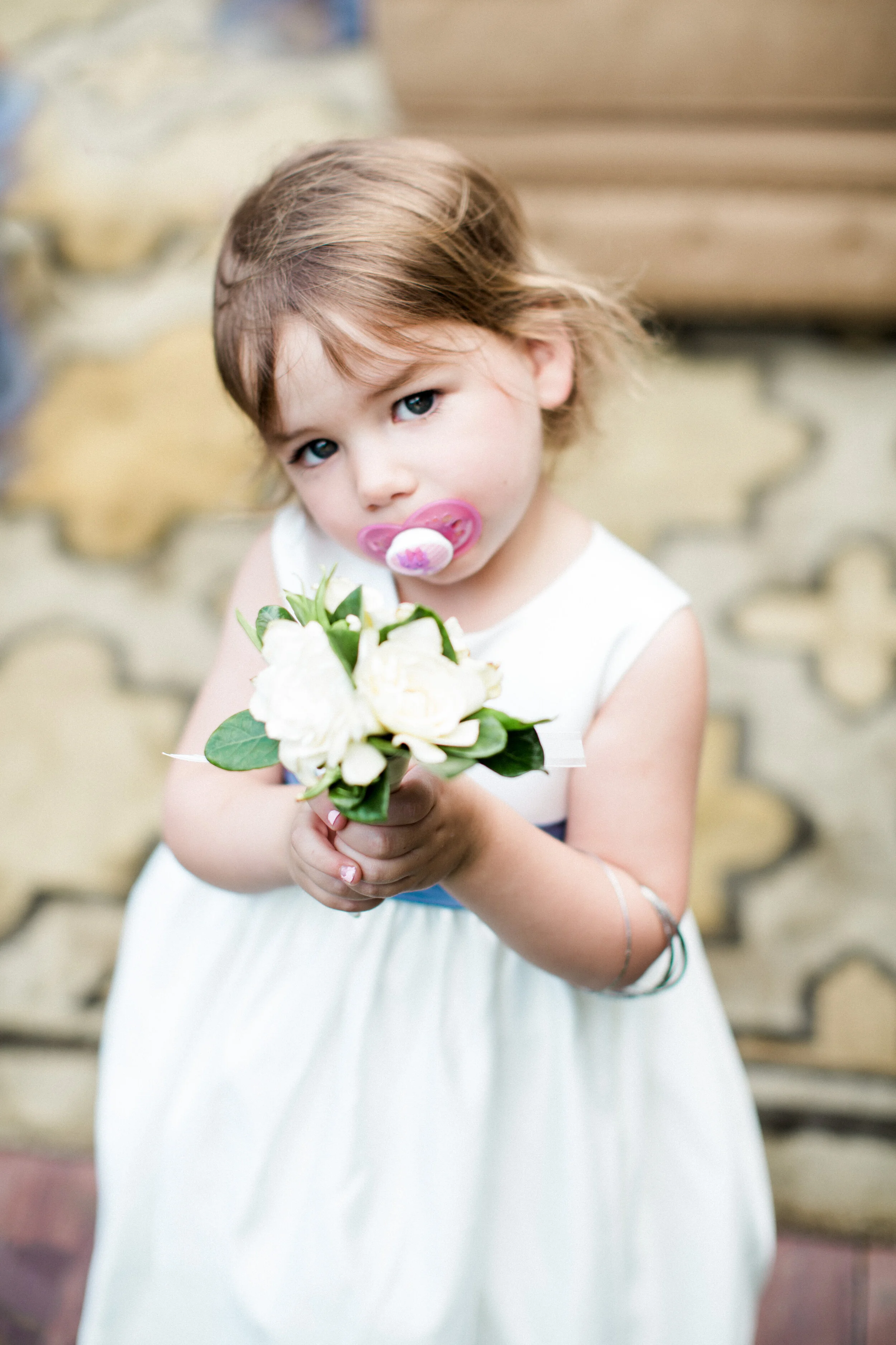 Young girl with a pacifier holding a bouquet of white flowers.