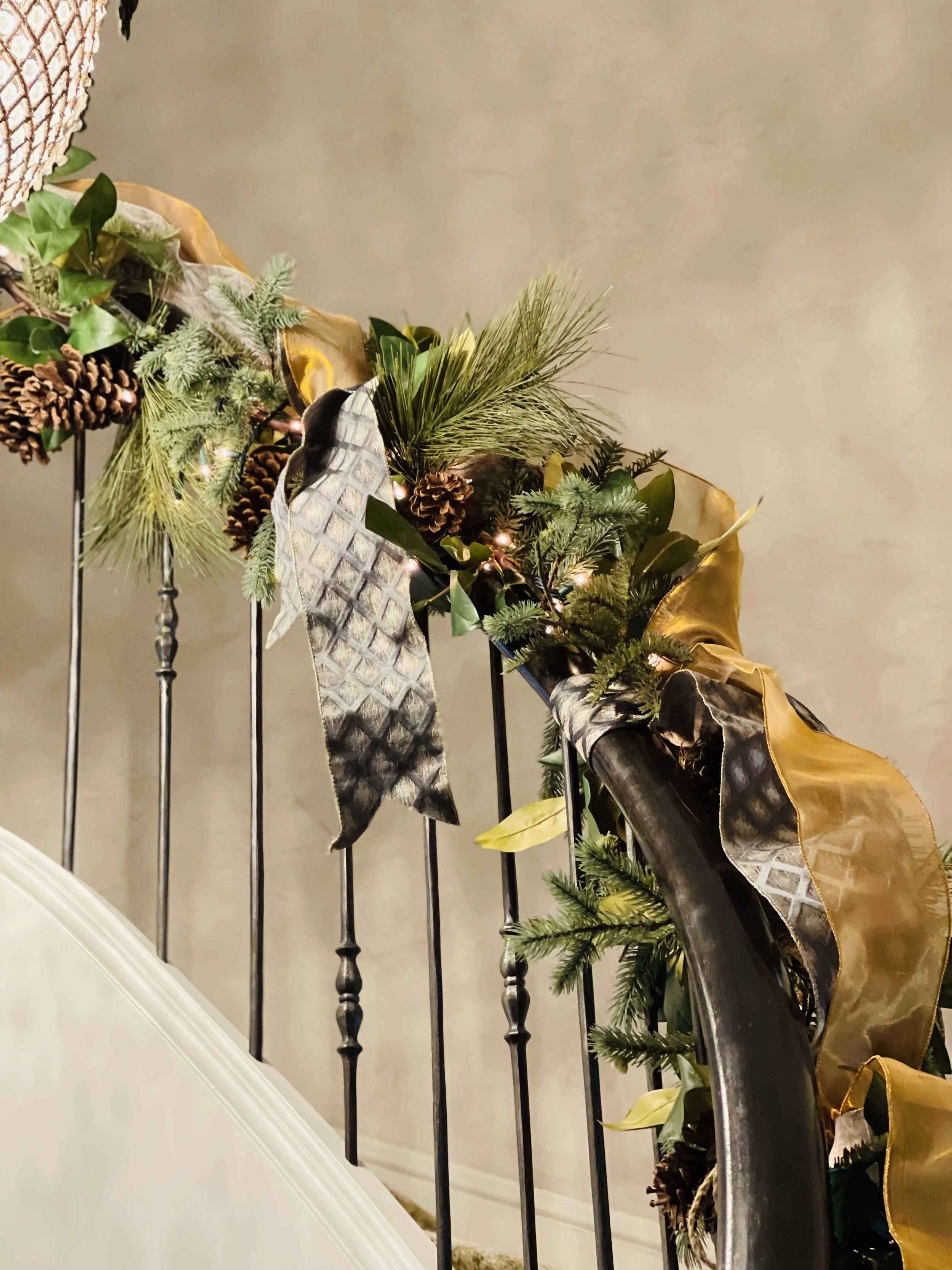 Close-up of a staircase railing decorated with holiday greenery, pinecones, and ribbons in gold, silver, and black.