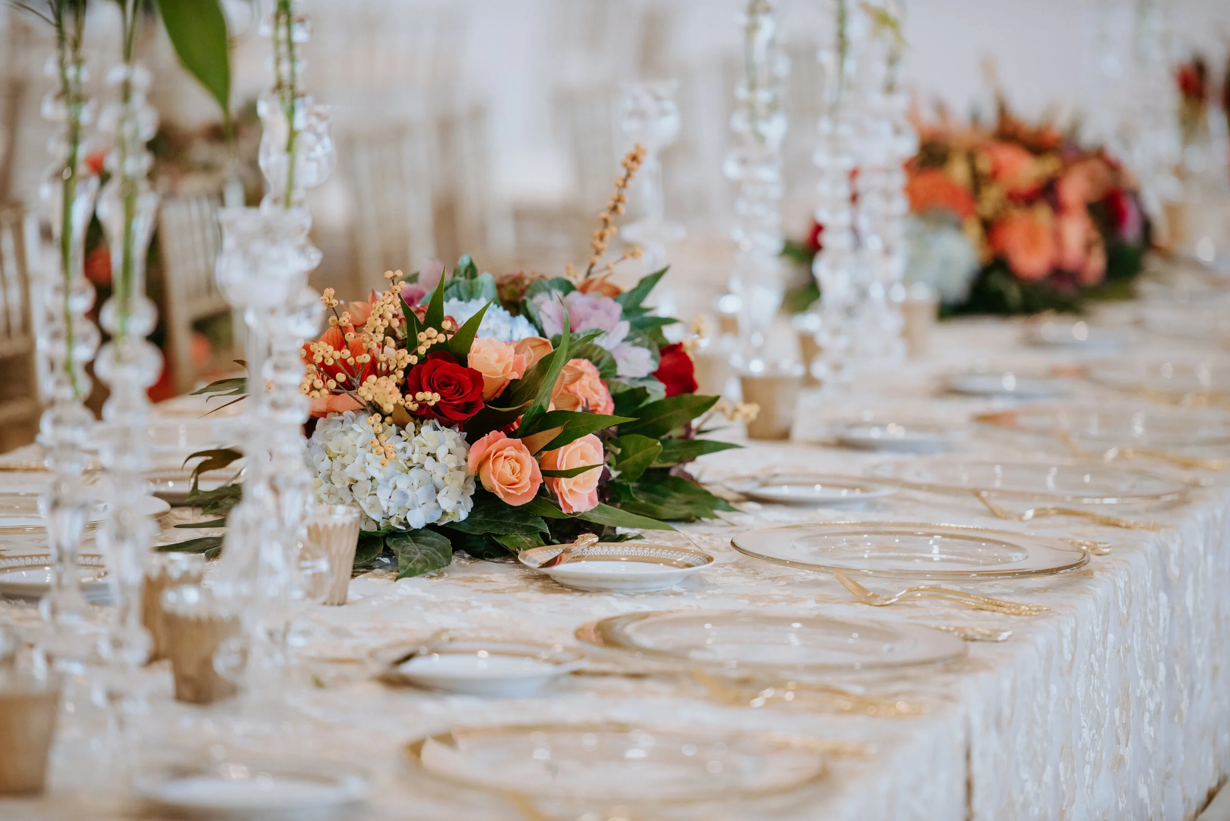 Elegant table setting with floral centerpiece, clear glass plates, and crystal candlesticks.