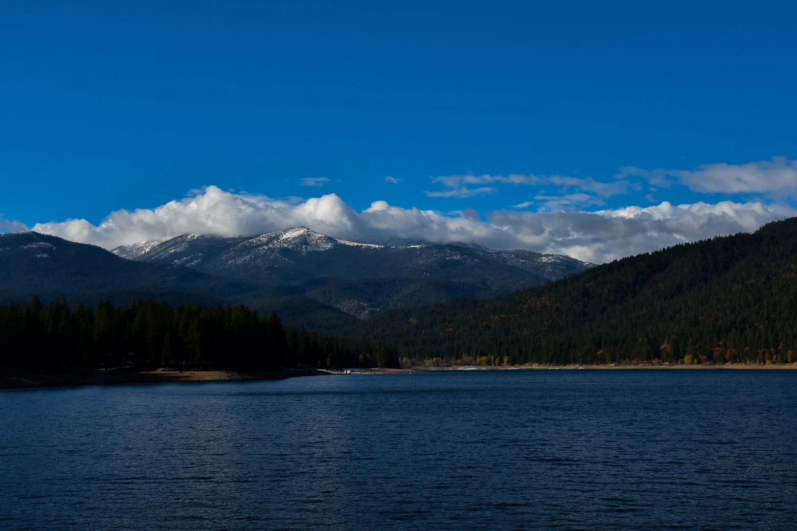 Mountain range with snow-capped peaks across a large body of water under a blue sky with clouds.