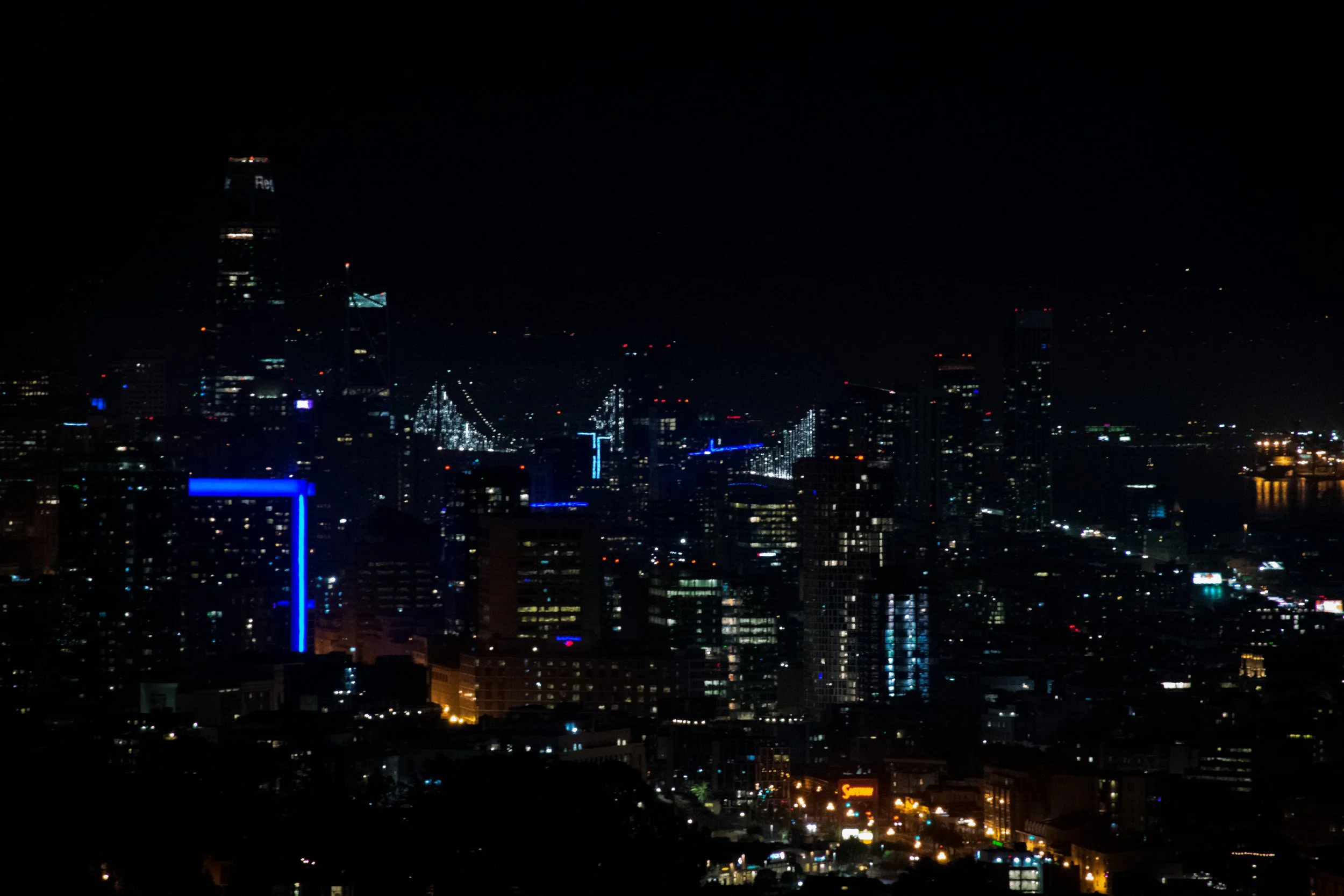 Nighttime city skyline with illuminated buildings and a bridge, dark sky.