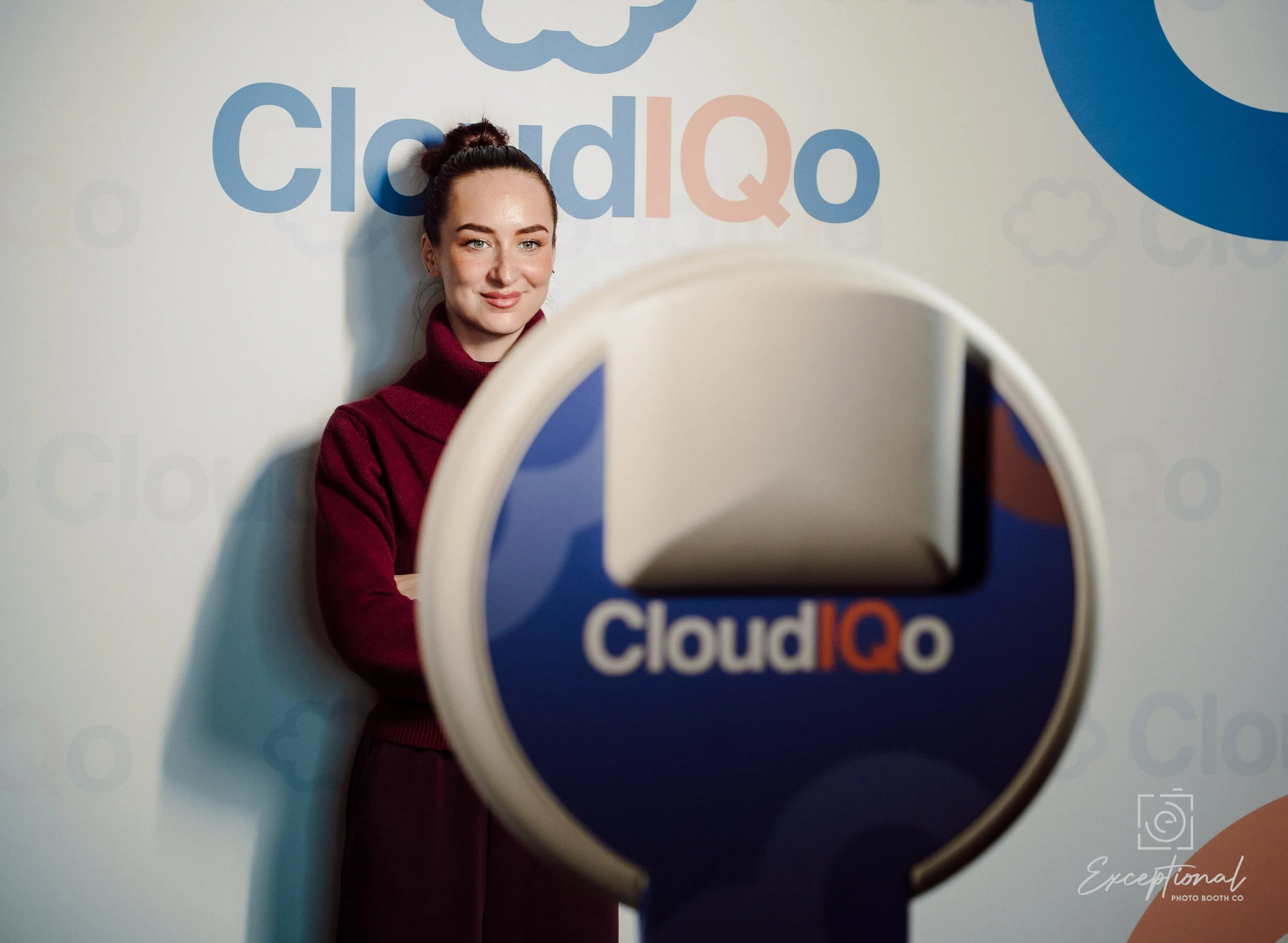 A woman standing in front of a wall with the 'CloudIQ' logo, with a sign in front of her displaying the same logo.