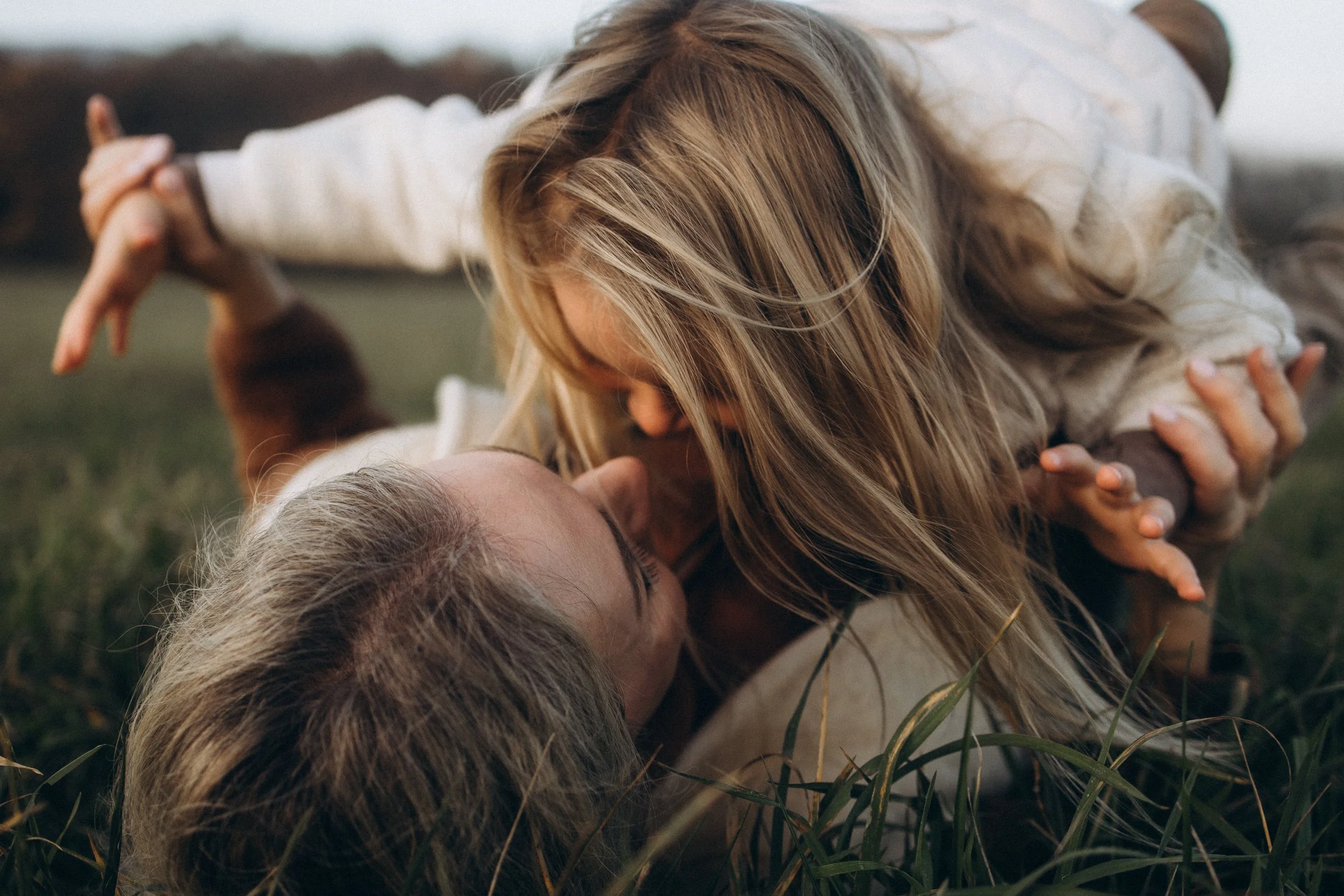 maminka s dcerou se svetlymi dlouhymi vlasy lezi a dovadeji na podzimni louce 