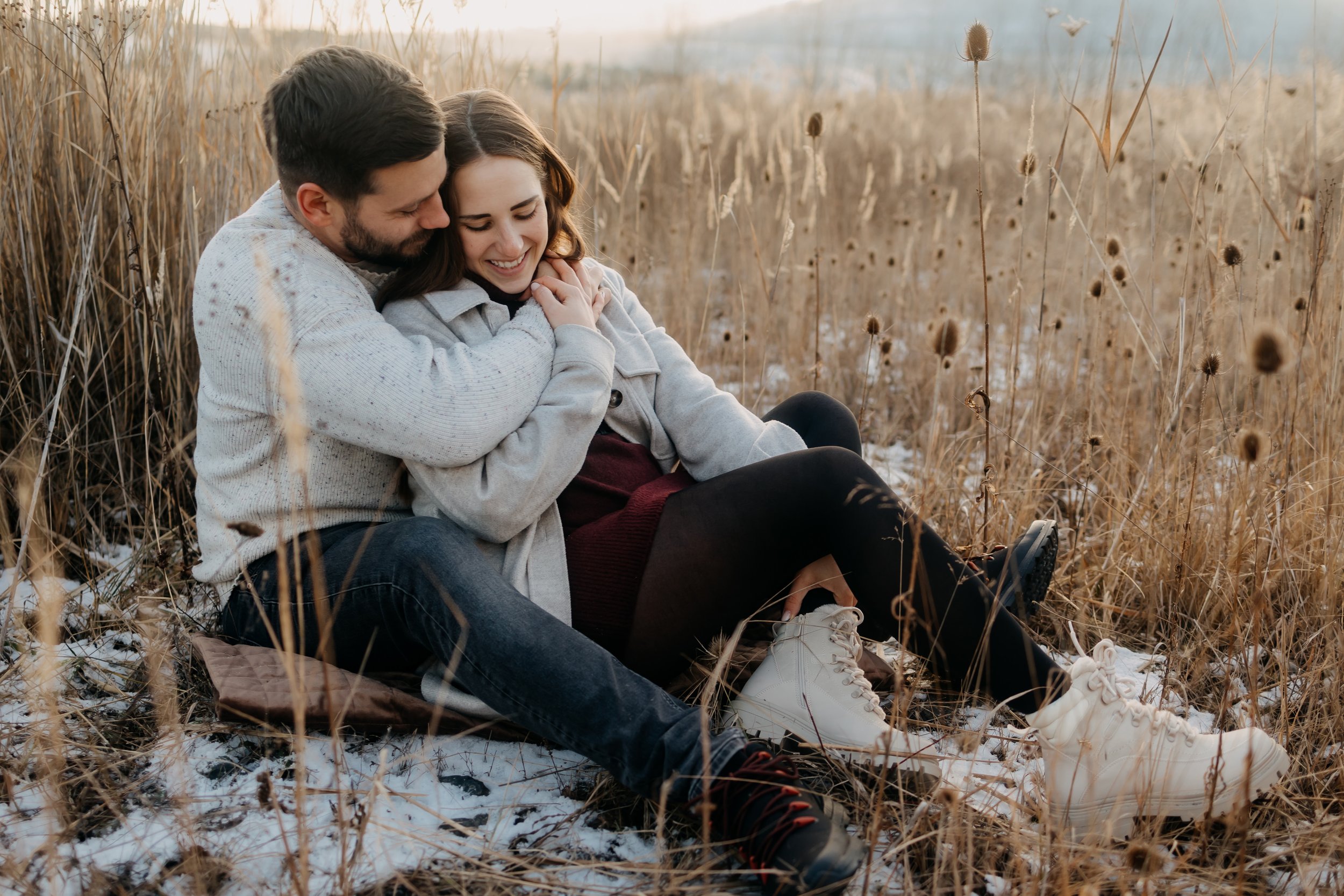 muz laskyplne objima zenu zatimco oba sedi na zemi v zimni krajine
