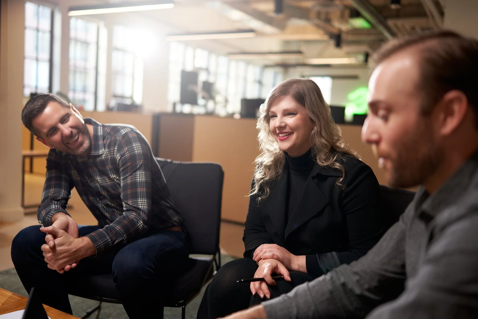 Three people sitting and laughing in an office or meeting room.