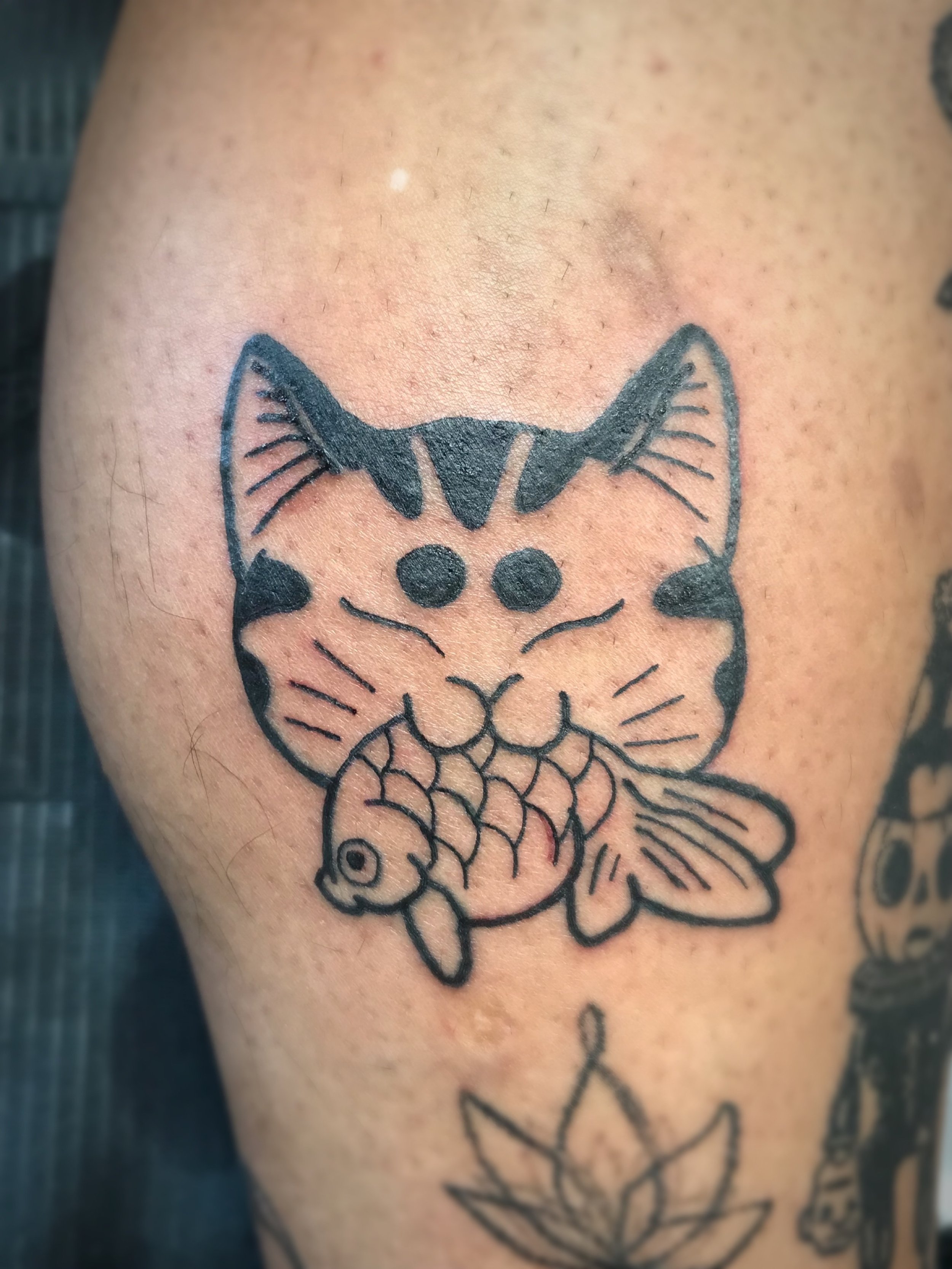 Tattoo of a cat face with a fish in its mouth