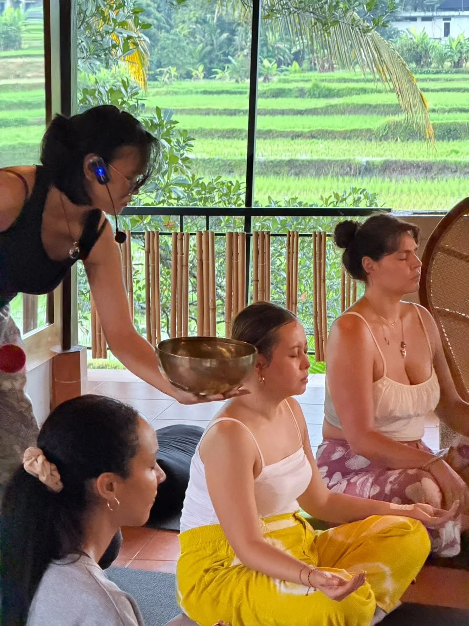 Women practicing meditation indoors with a scenic rice paddy view outside the window.