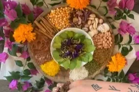 Arrangement of various herbs, spices, and flowers on a decorative tray with a small bowl of leafy greens and colorful flowers surrounding it.