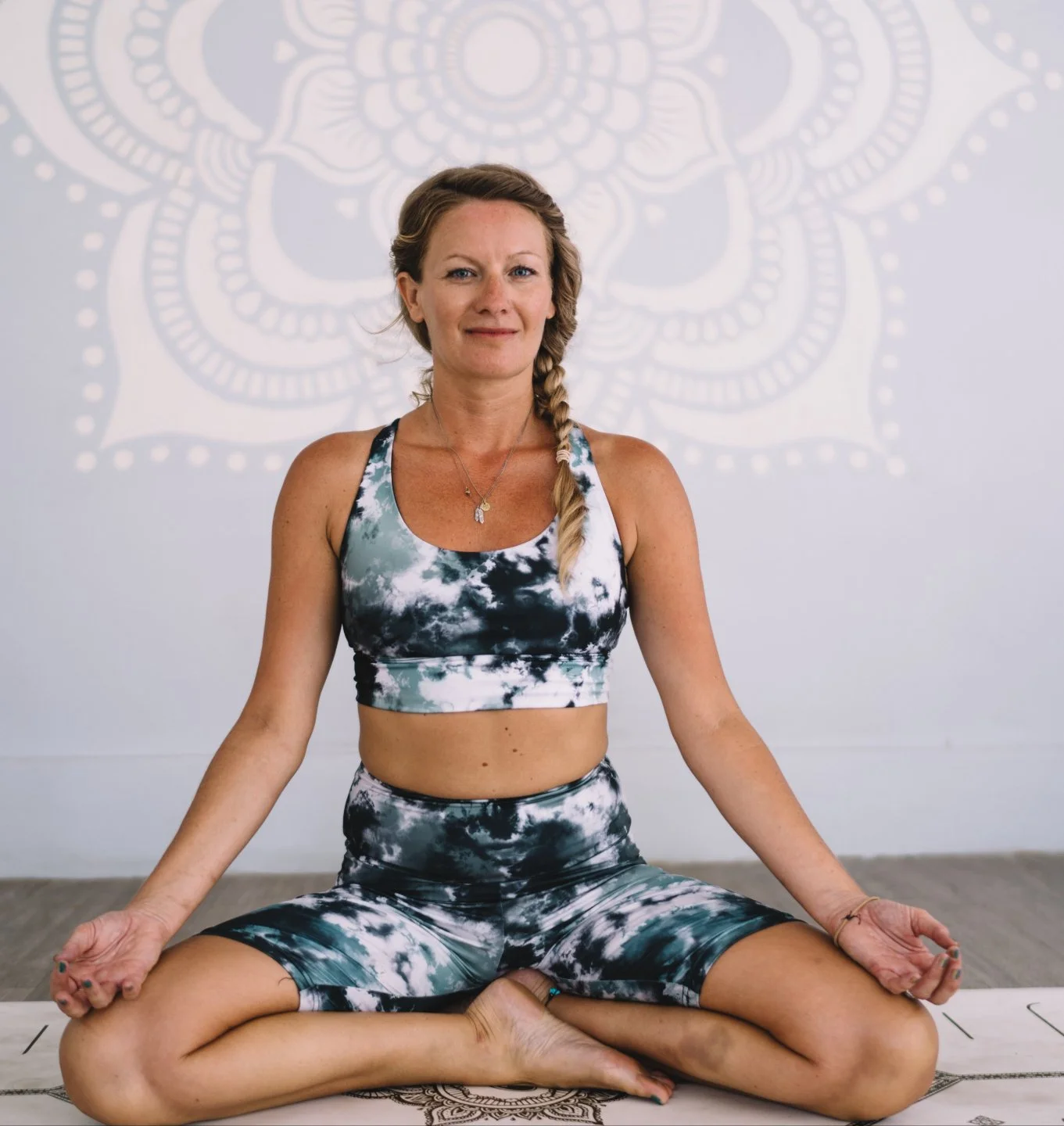 A woman practicing yoga in a seated meditation pose on a yoga mat with a decorative background design.