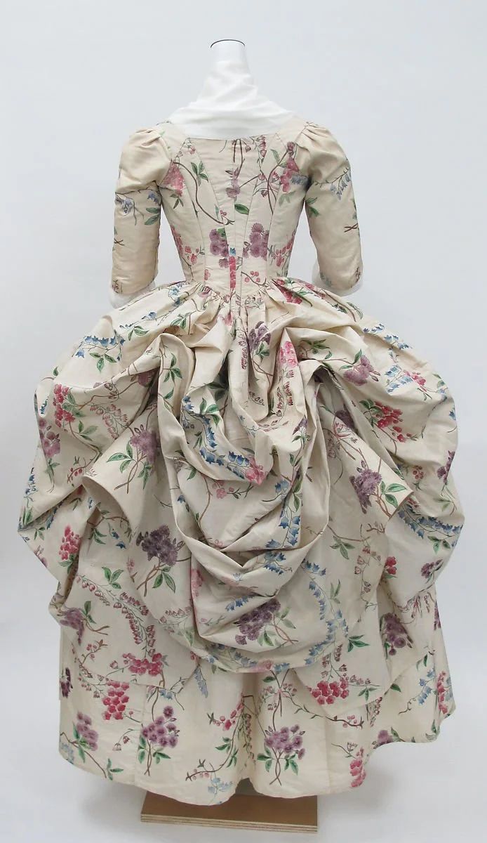 A vintage floral gown with a full skirt and puffed sleeves displayed from the back on a mannequin.