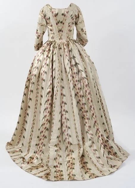 A vintage-style gown with a full skirt and long sleeves, featuring a cream base with pink, green, and black patterned stripes and designs.