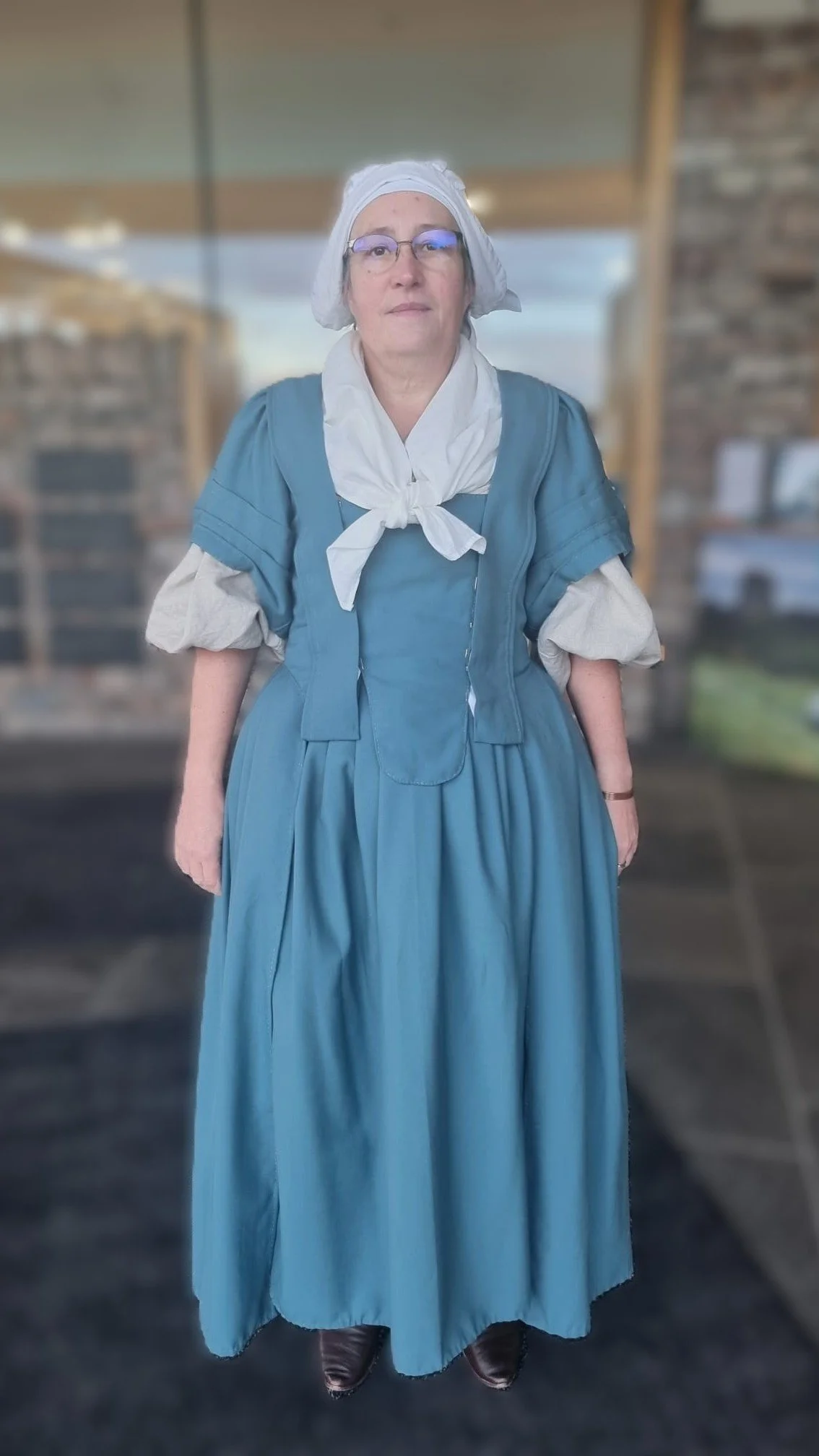 Tania modelling the new 1740s gown she made in one of Rebecca's gown-making workshops. Her gown is made of a sea blue worsted wool. She is also wearing her linen shift, handkerchief and cap, along with black shoes. This is the back view.