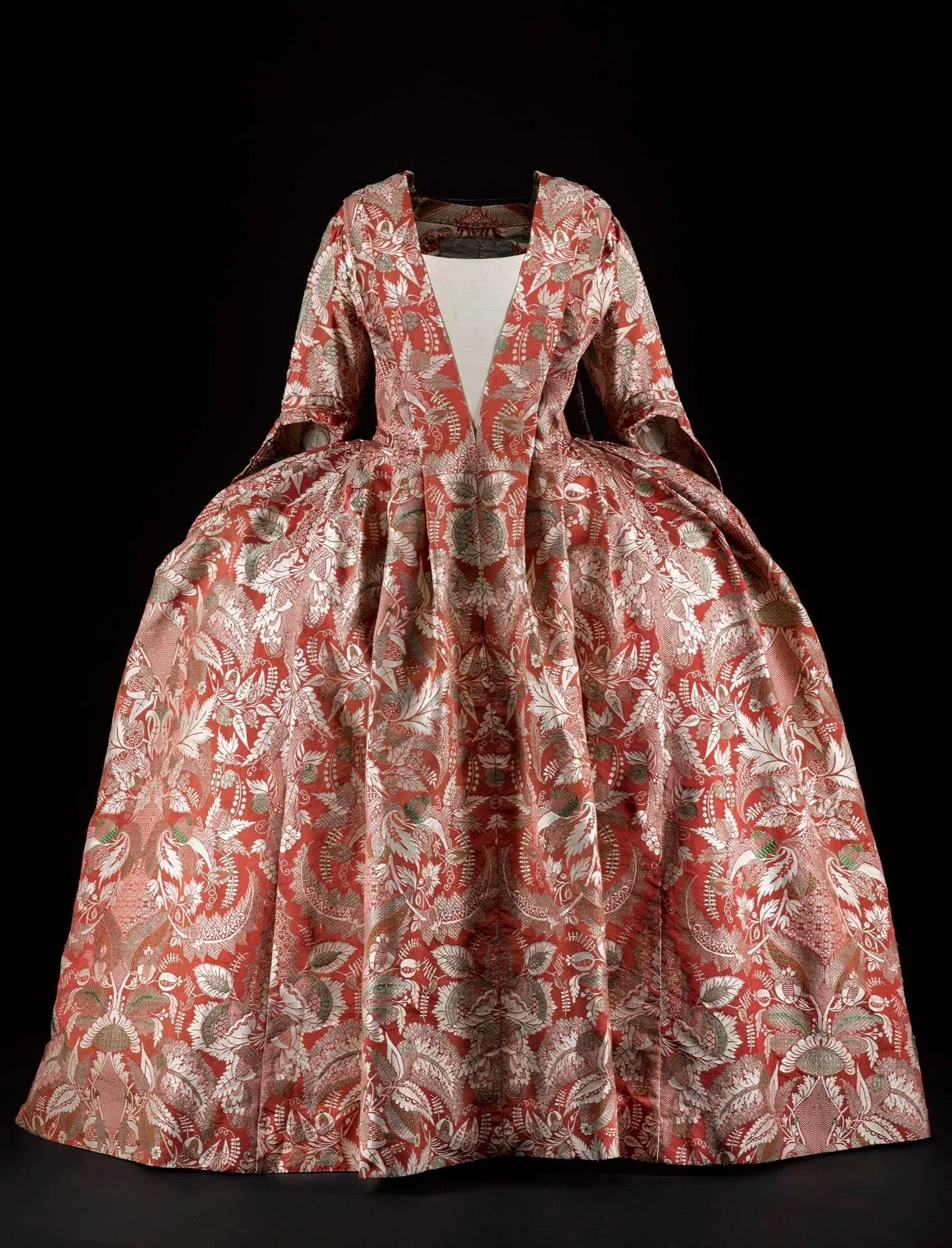 A vintage dress with a red and white floral and leaf pattern, long sleeves, and a full skirt, displayed on a black background.