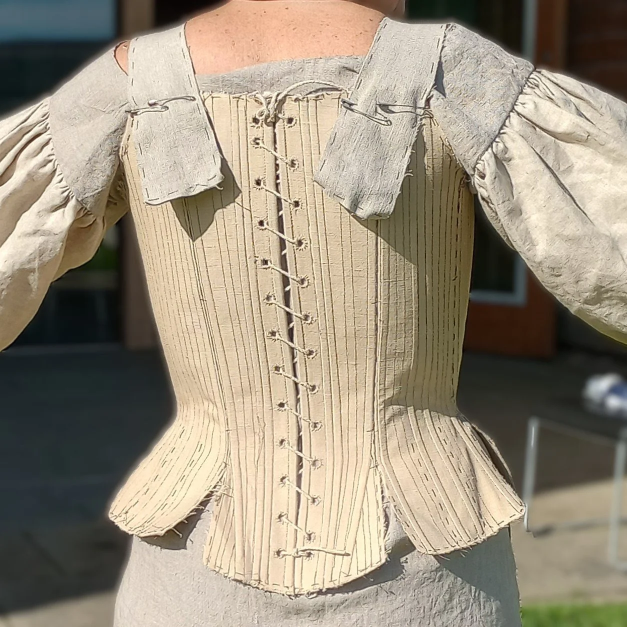 Tania stands outdoors wearing the first mock-up for her new 1740s stays, made from the custom arc-method pattern drafted by Rebecca. This is the back view.
