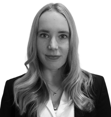 Black and white portrait of a woman with long wavy blonde hair, wearing a blazer and a necklace, looking at the camera with a neutral expression.