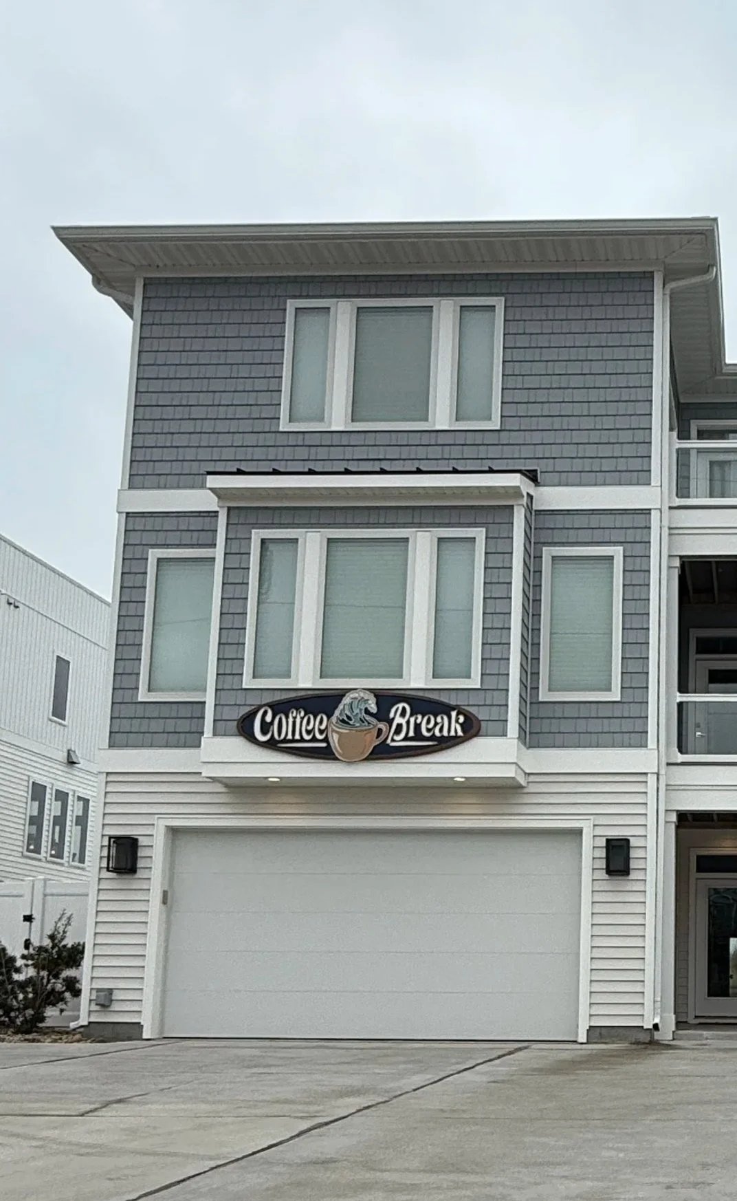 A modern multi-story building with a sign that reads 'Coffee Break' featuring a steaming coffee cup logo. The building has light gray siding and large windows.