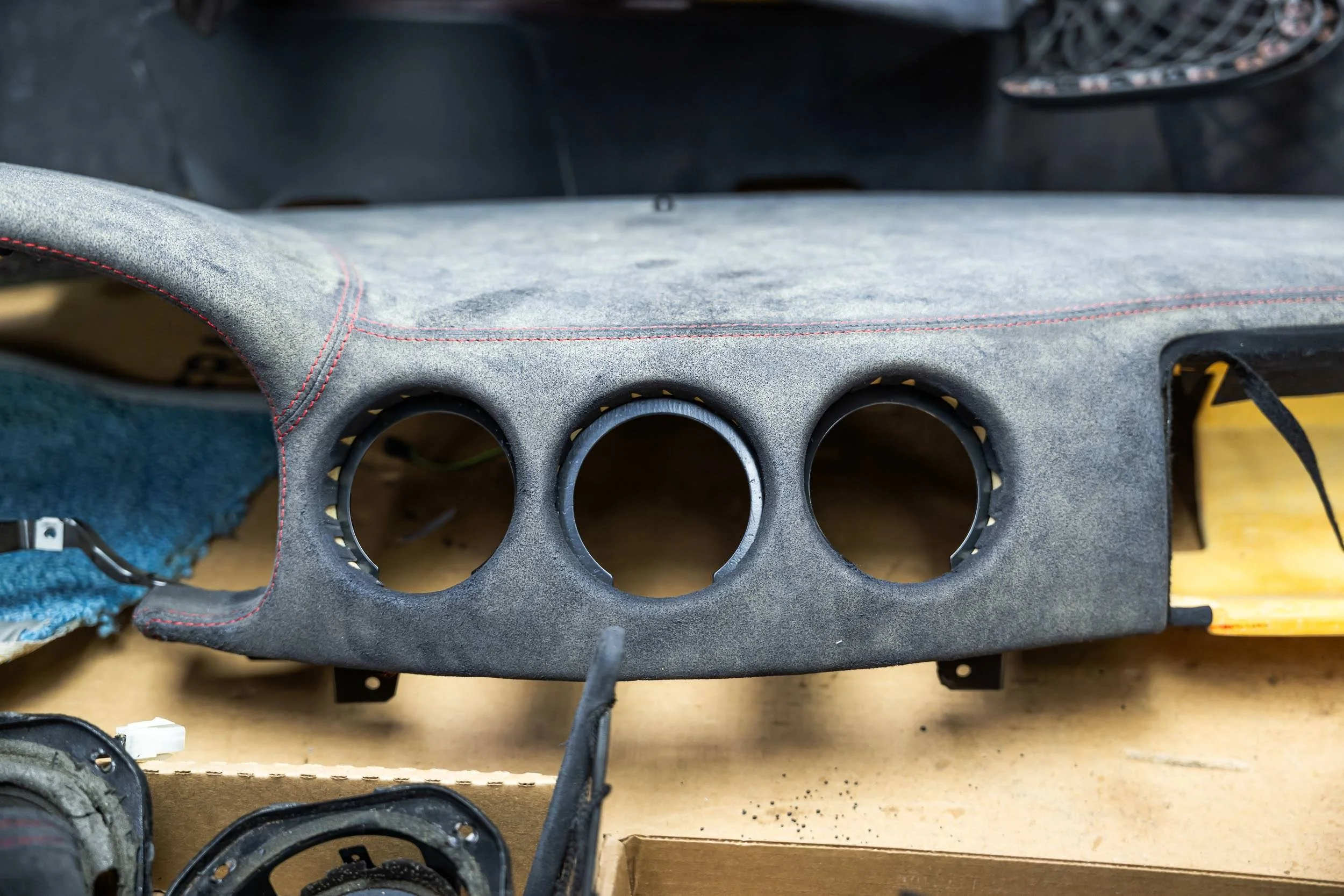 Close-up photo of a cardboard box containing a used car speaker mounting panel with three circular holes, some wiring, and a textured gray surface.