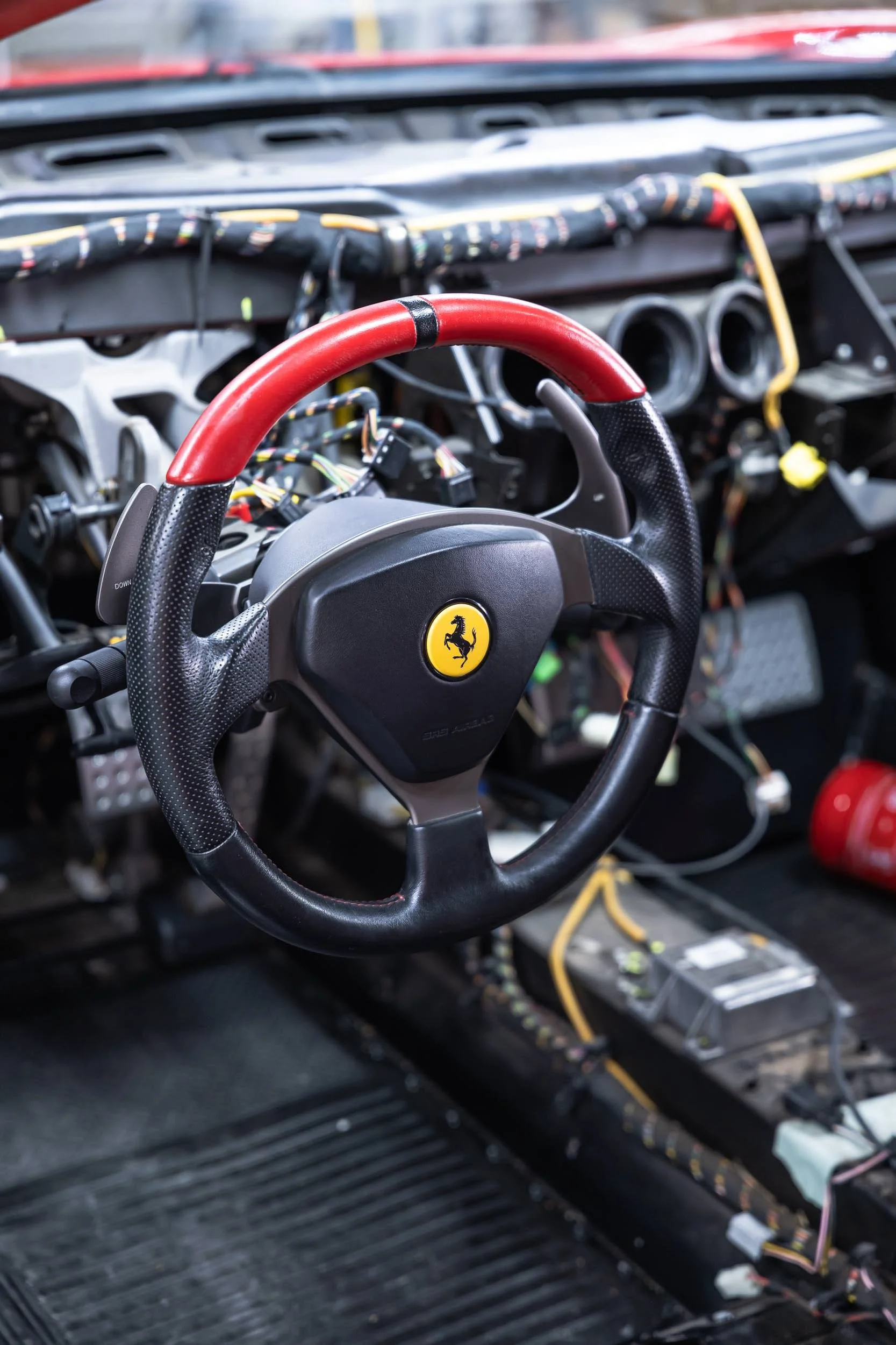 Interior of a race car with a black steering wheel featuring a yellow Ferrari logo, and visible wiring and dashboard disassembly.