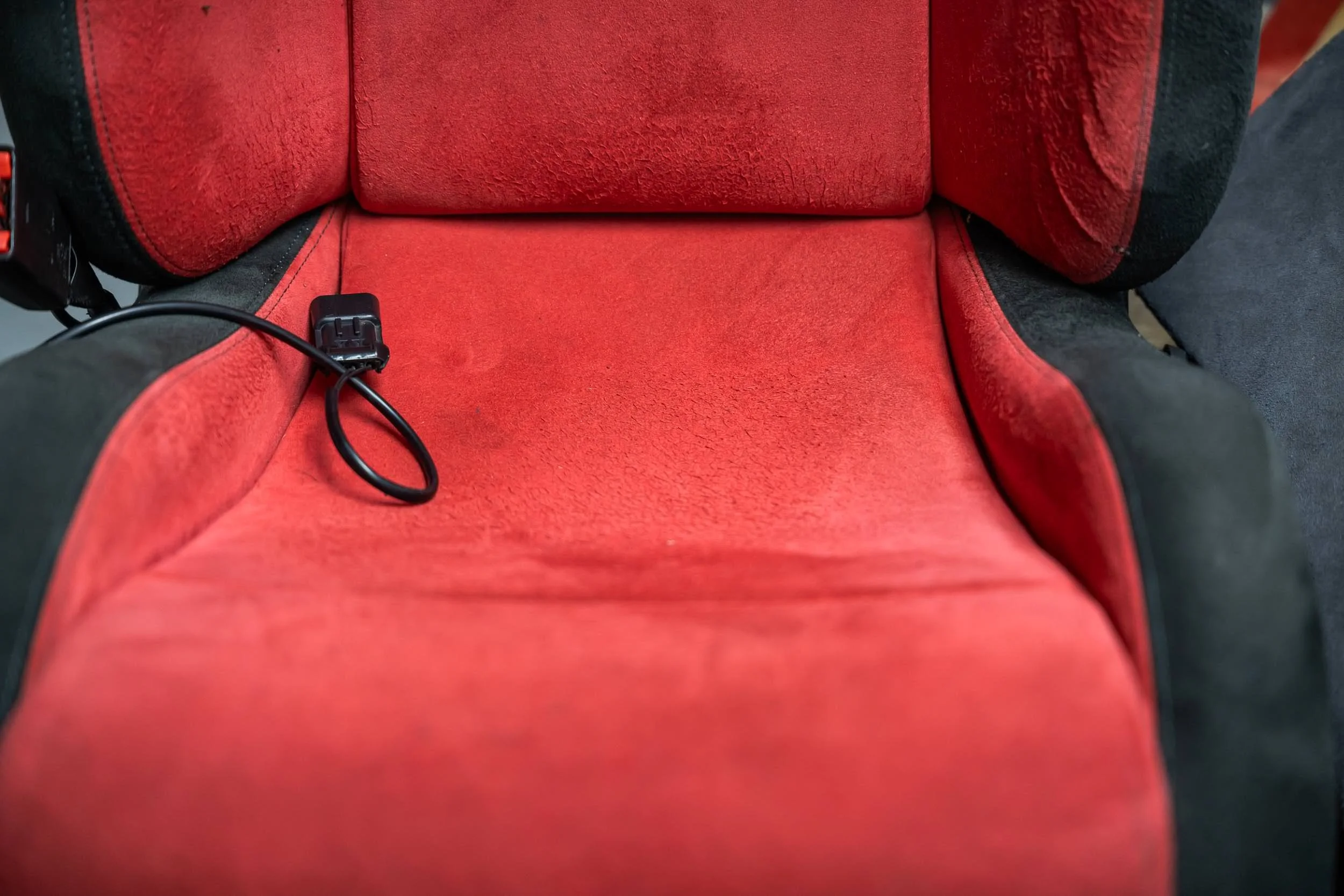 Close-up of the interior of a red and black car seat with some electrical wiring visible.