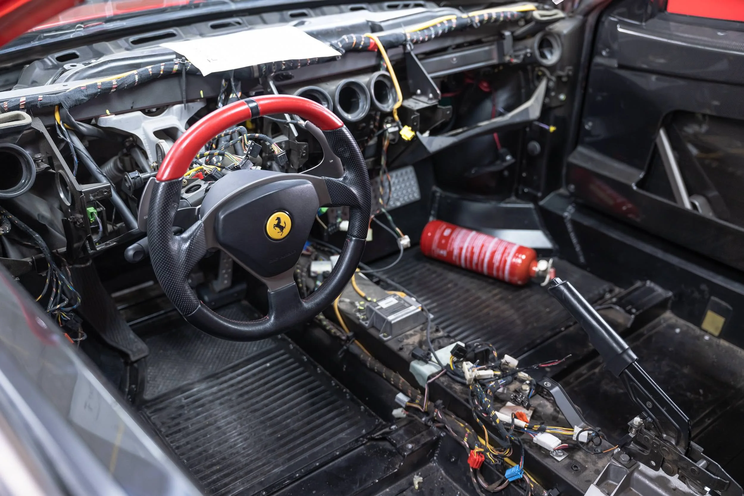 The interior of a Ferrari race car with the dashboard and steering wheel visible, and the interior paneling removed, exposing the car's wiring and mechanical components.